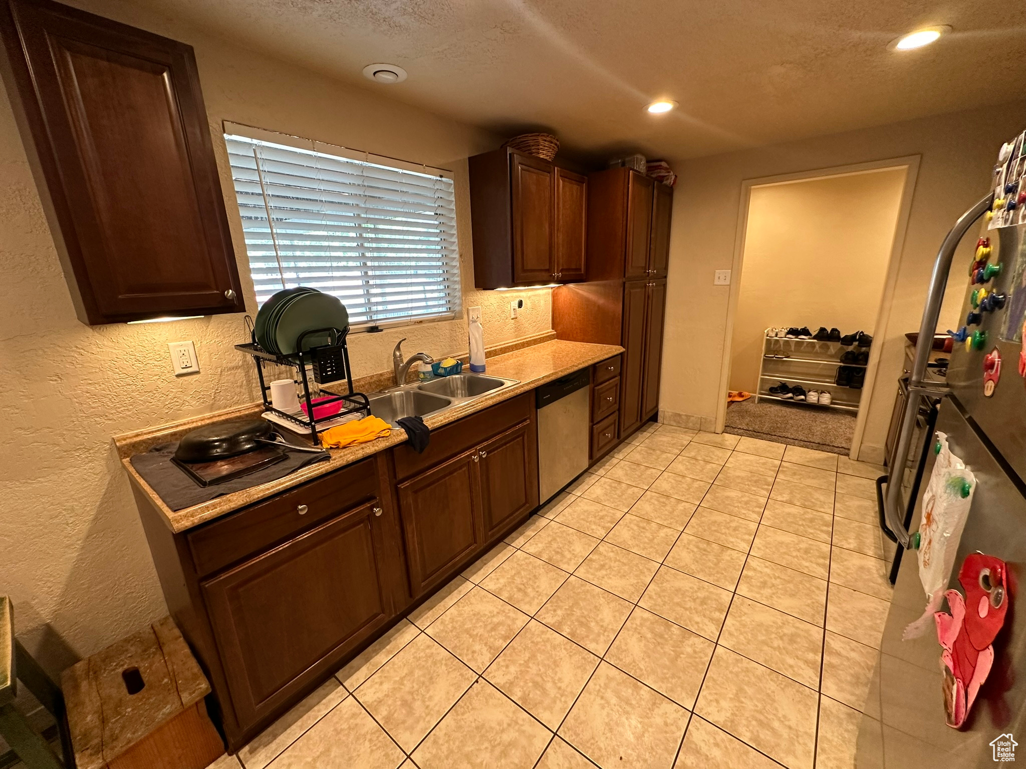 Kitchen with sink, dark brown cabinets, light tile flooring, and stainless steel dishwasher