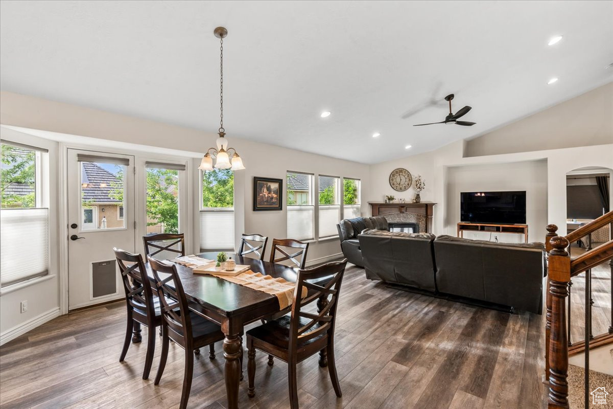 Dining area featuring ceiling fan with notable chandelier, dark hardwood / wood-style flooring, vaulted ceiling, and a wealth of natural light