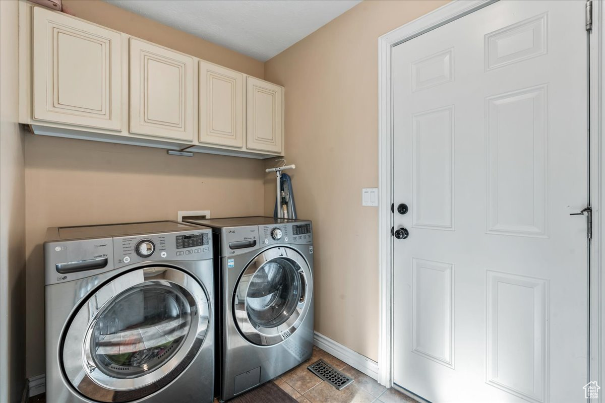 Laundry area featuring independent washer and dryer, light tile patterned floors, and cabinets