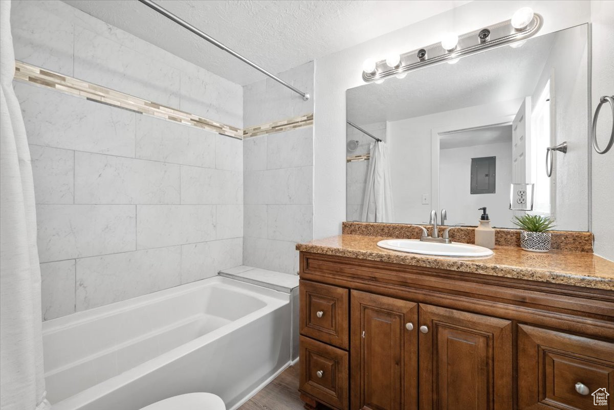 Bathroom with a textured ceiling, shower / bath combination with curtain, vanity, and wood-type flooring