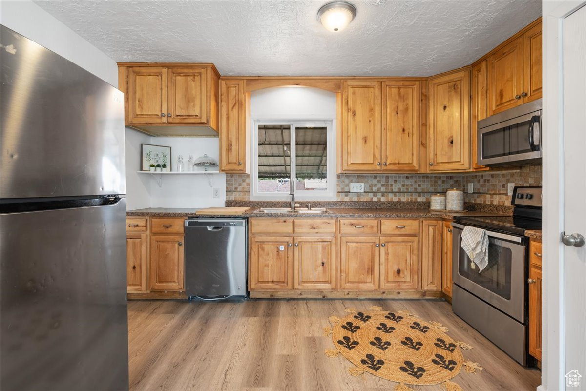 Kitchen with tasteful backsplash, light wood-type flooring, appliances with stainless steel finishes, and sink