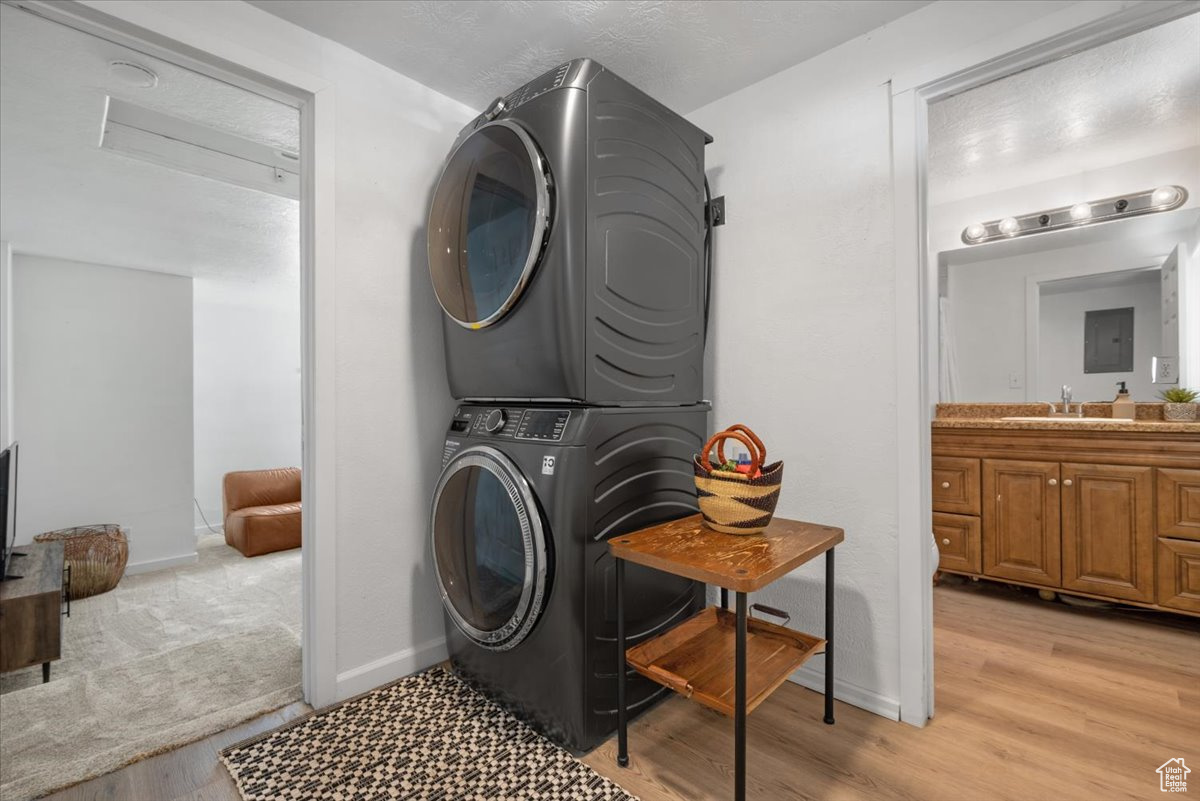 Clothes washing area with stacked washer / dryer, light wood-type flooring, and sink