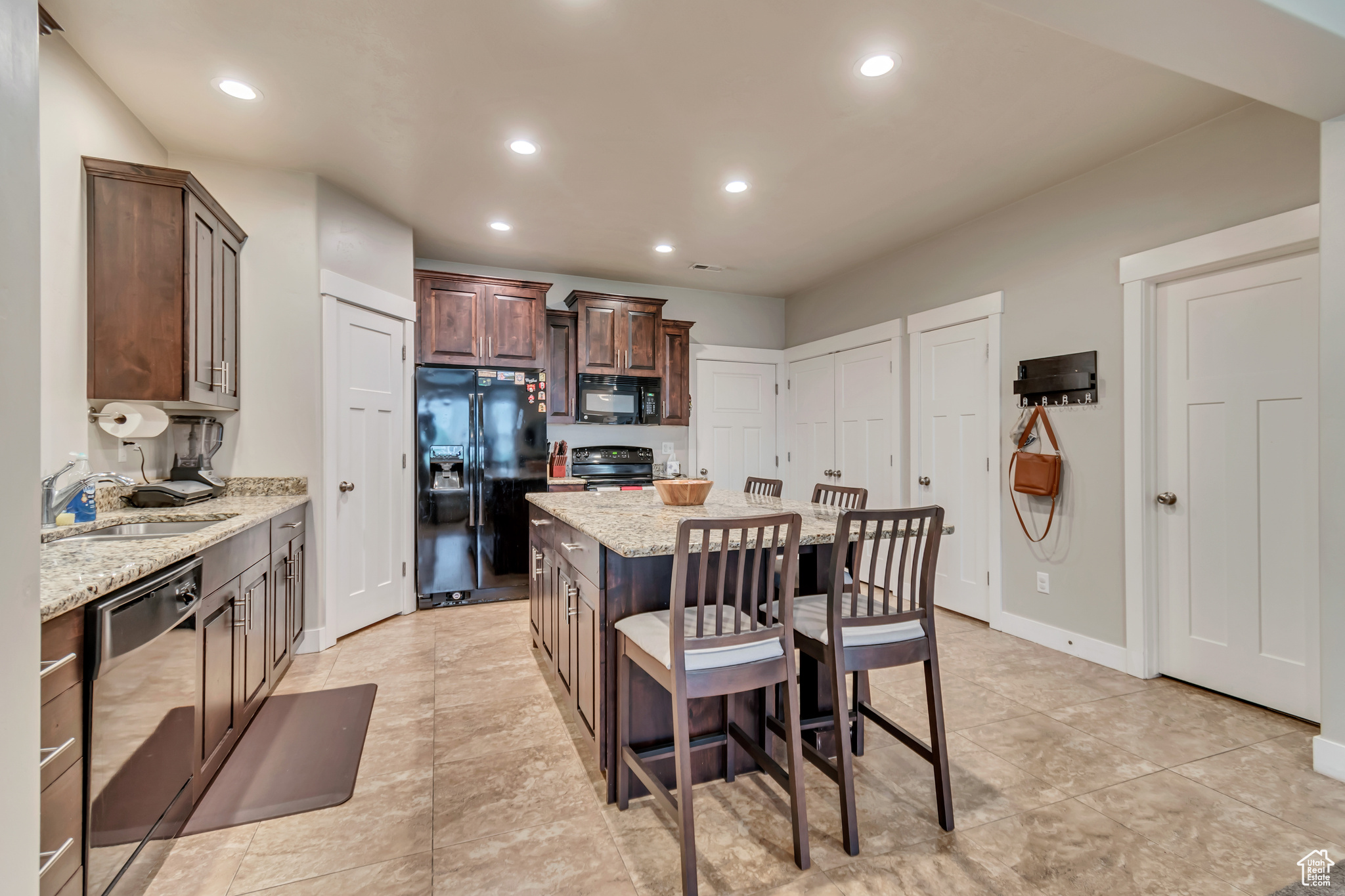 Kitchen featuring light tile patterned floors, a center island, light stone counters, and black appliances