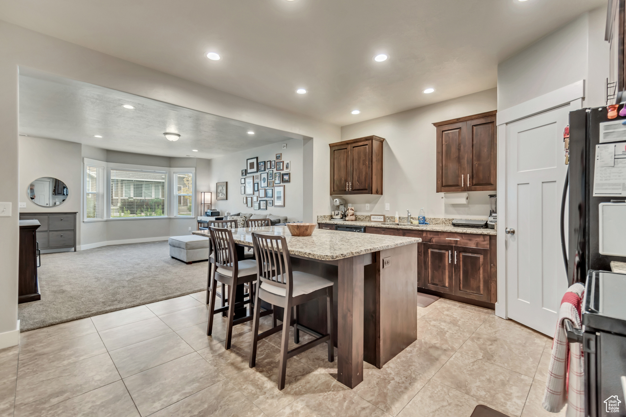 Kitchen featuring a kitchen island, black fridge, light carpet, a breakfast bar, and light stone countertops