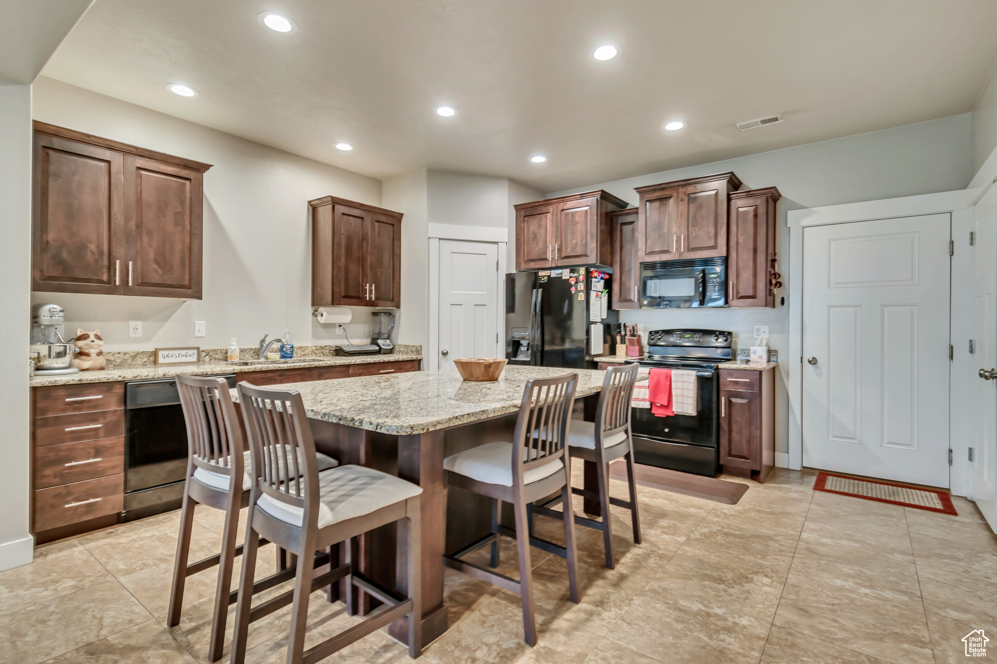 Kitchen featuring light stone counters, black appliances, a breakfast bar area, a center island, and light tile patterned flooring