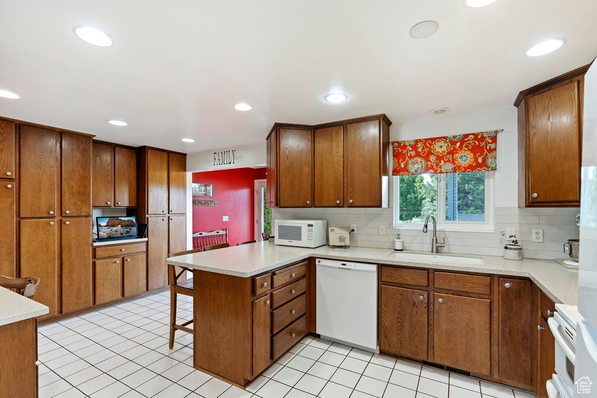 Kitchen with backsplash, light tile patterned floors, sink, kitchen peninsula, and white appliances