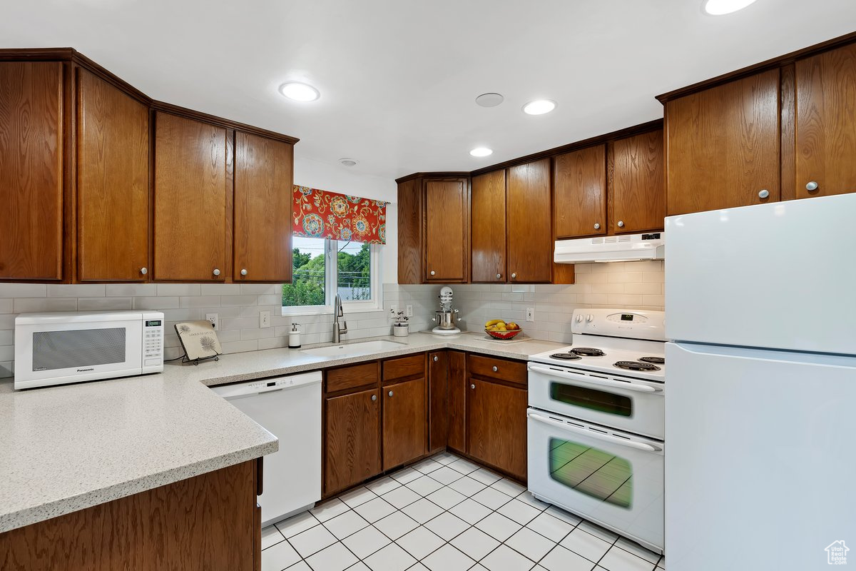 Kitchen with sink, white appliances, light tile patterned flooring, and tasteful backsplash