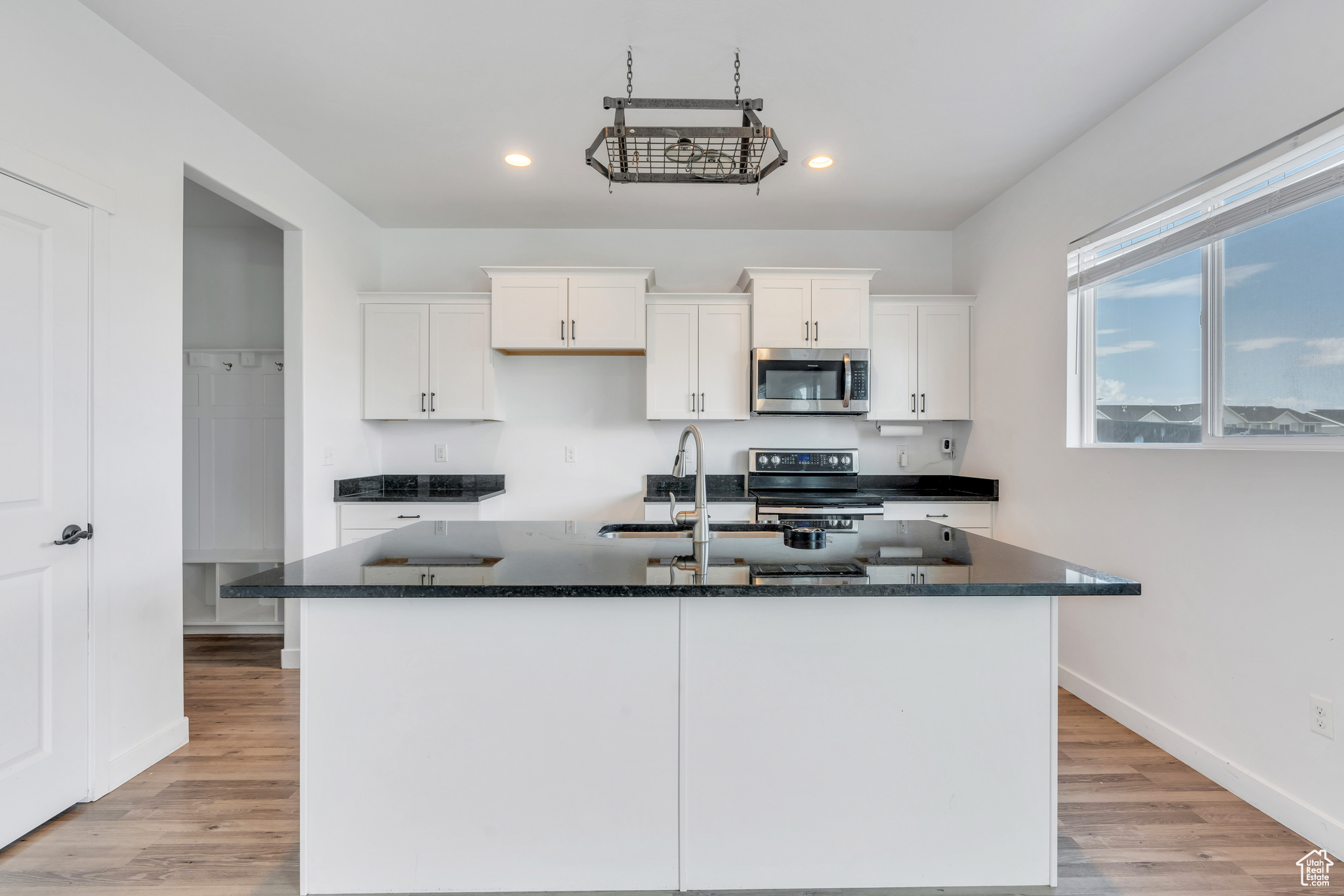 Kitchen with light hardwood / wood-style flooring, white cabinetry, sink, range with electric cooktop, and an island with sink