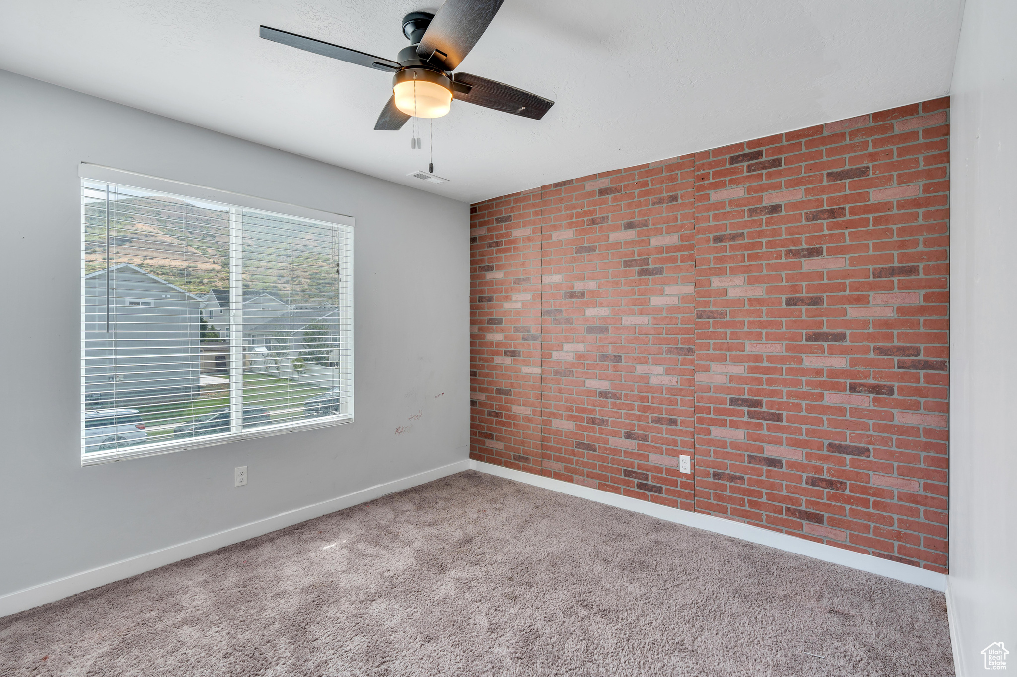 Empty room with ceiling fan, brick wall, and light carpet