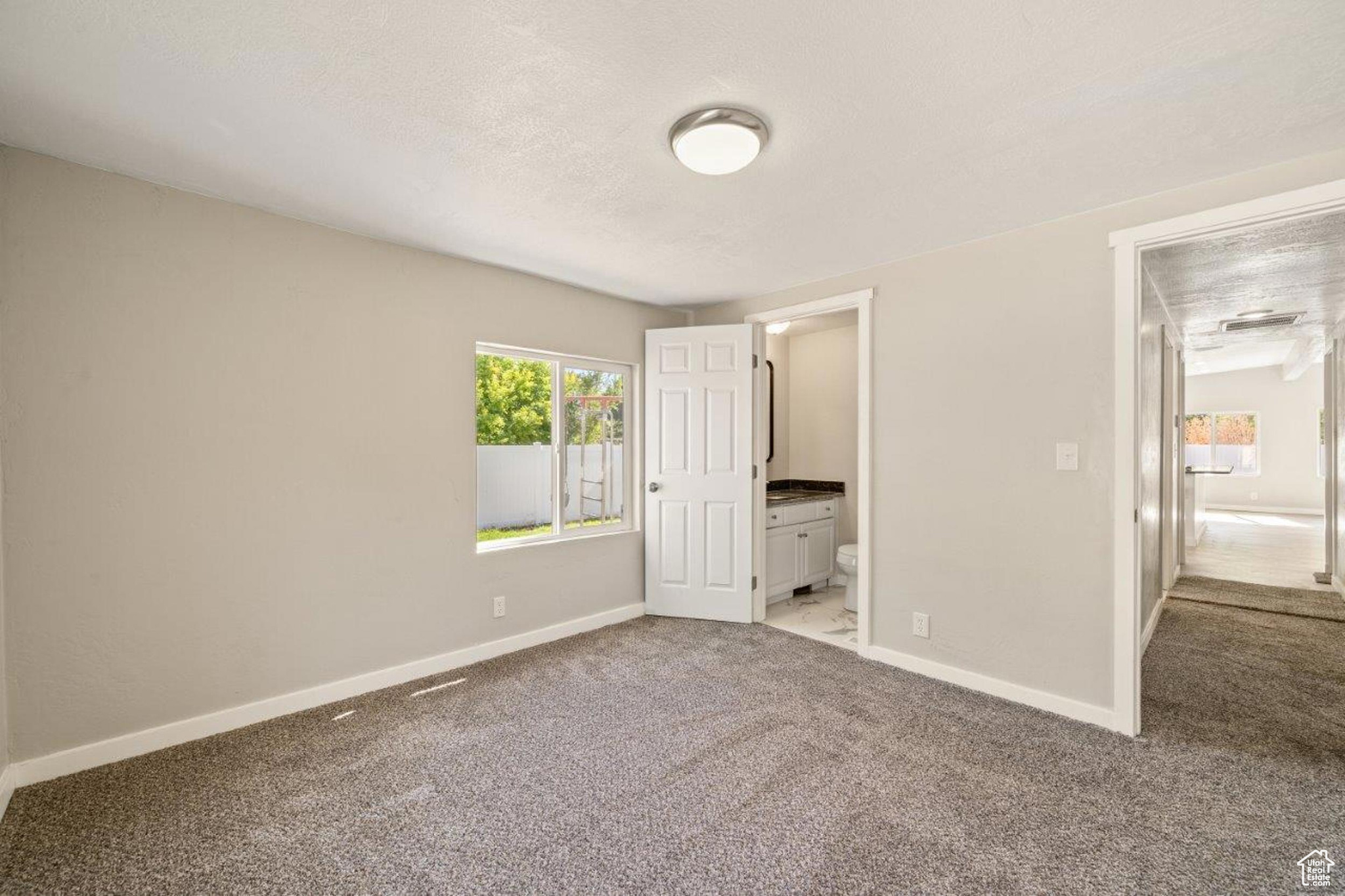 Unfurnished bedroom featuring light colored carpet, ensuite bathroom, and a textured ceiling