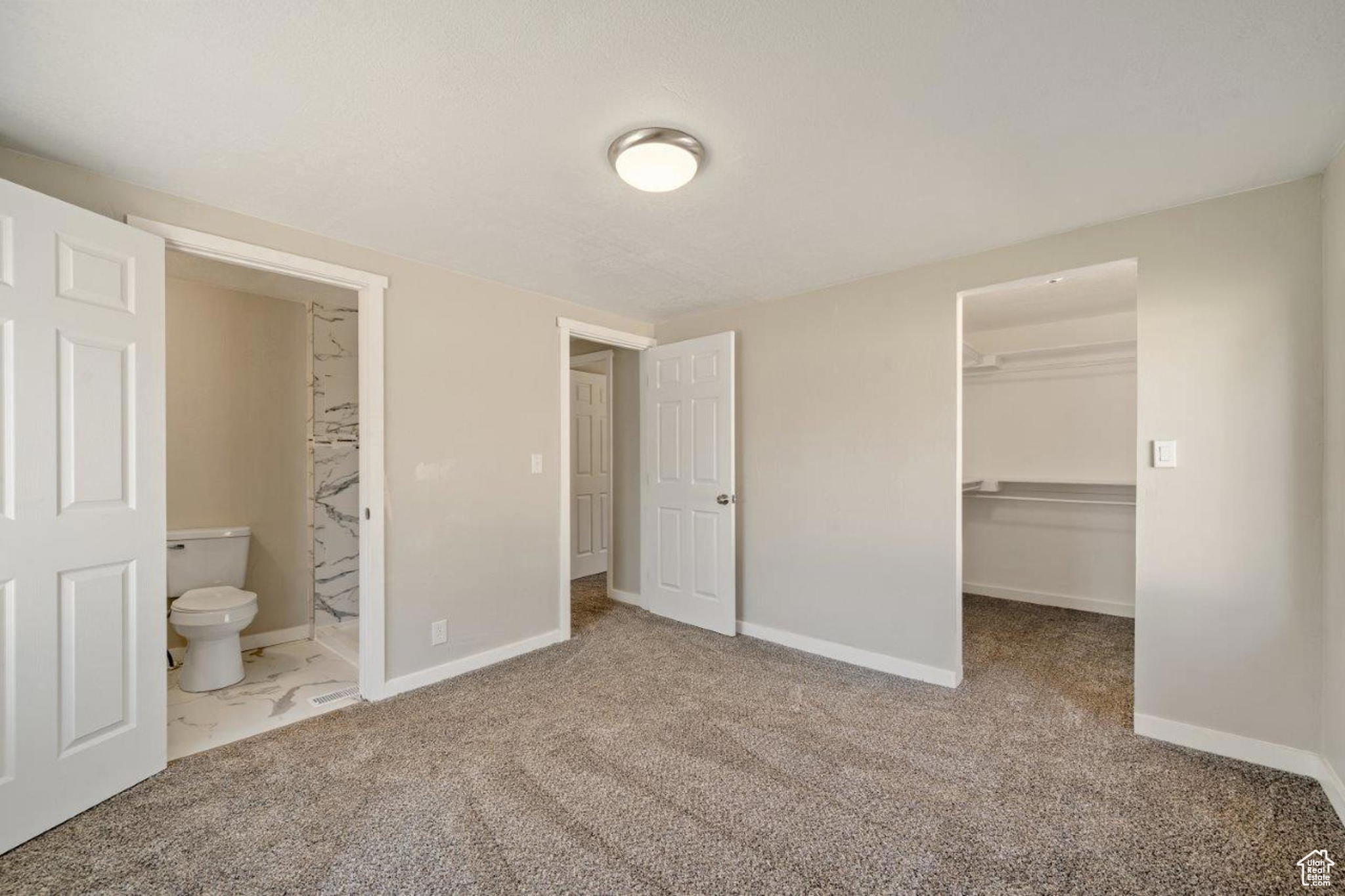 Unfurnished bedroom featuring carpet flooring, a spacious closet, a closet, and ensuite bathroom