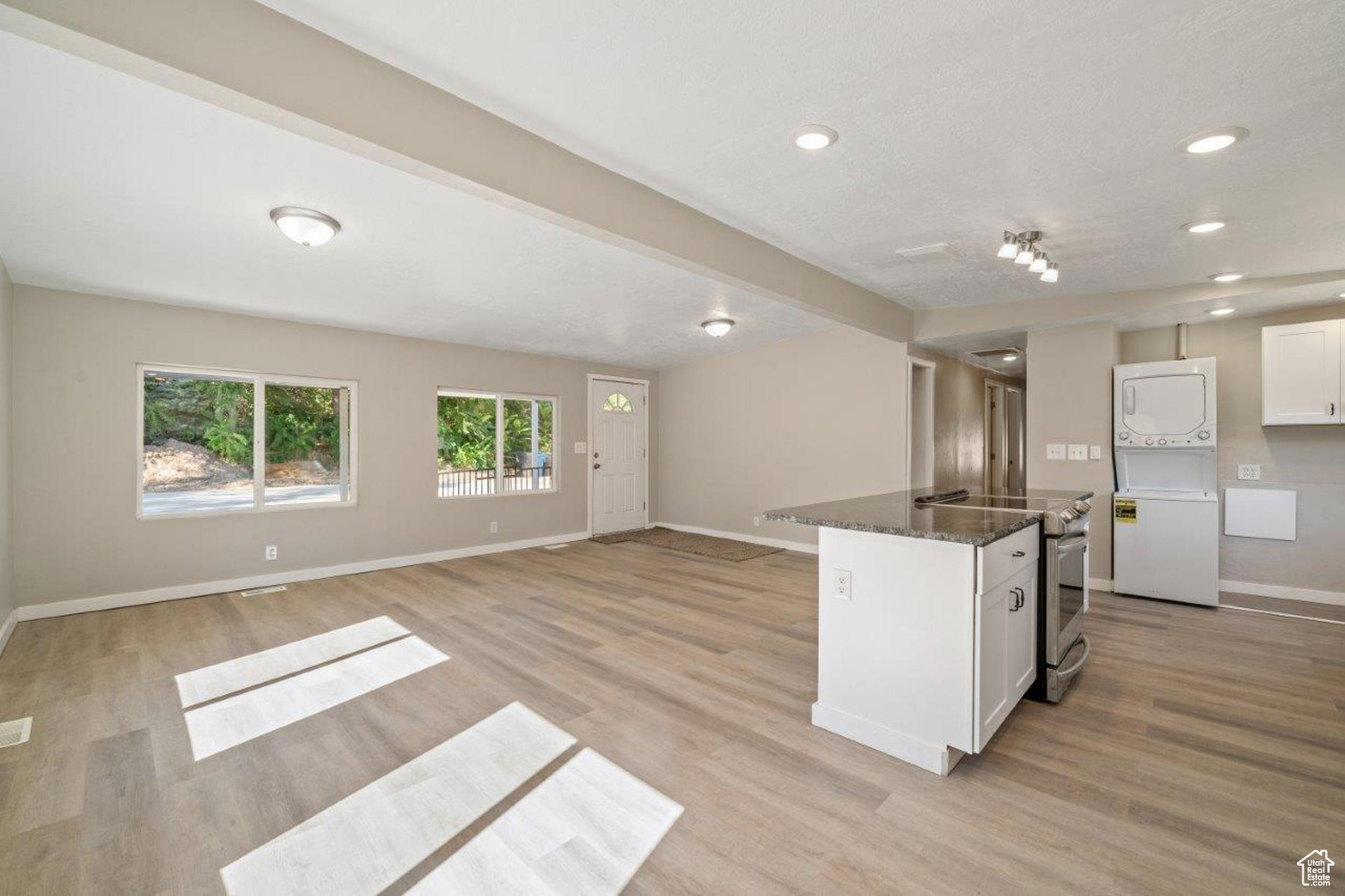 Kitchen with light wood-type flooring, stacked washer and dryer, stainless steel electric stove, and white cabinets