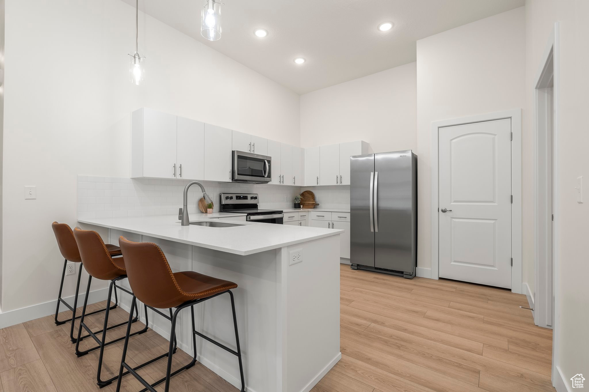 Kitchen featuring white cabinetry, sink, hanging light fixtures, stainless steel appliances, and light hardwood / wood-style floors