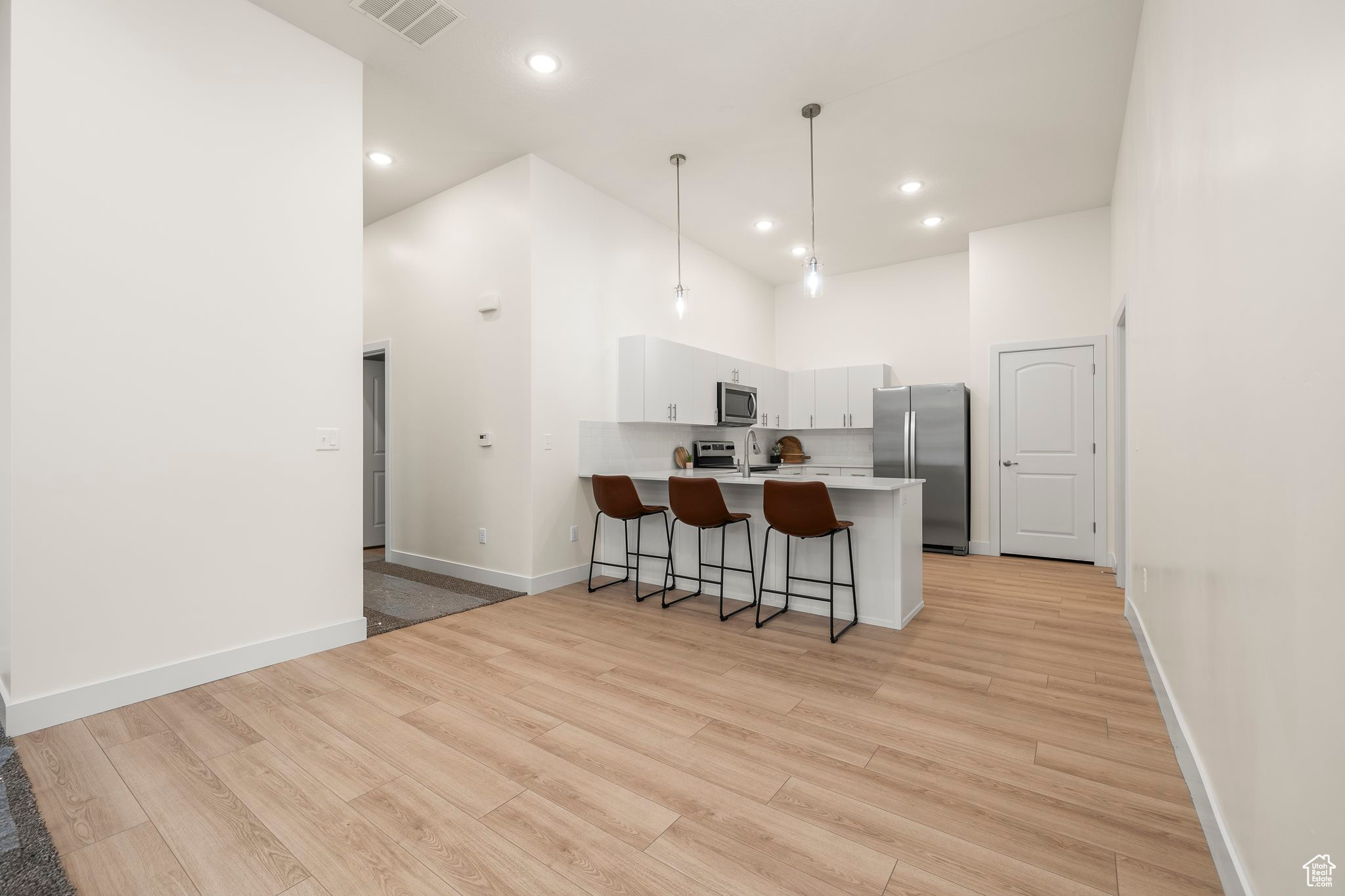 Kitchen with kitchen peninsula, a high ceiling, stainless steel appliances, and white cabinetry