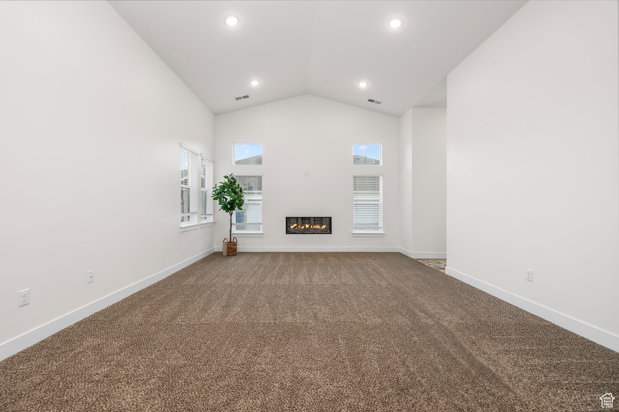 Unfurnished living room featuring carpet and vaulted ceiling