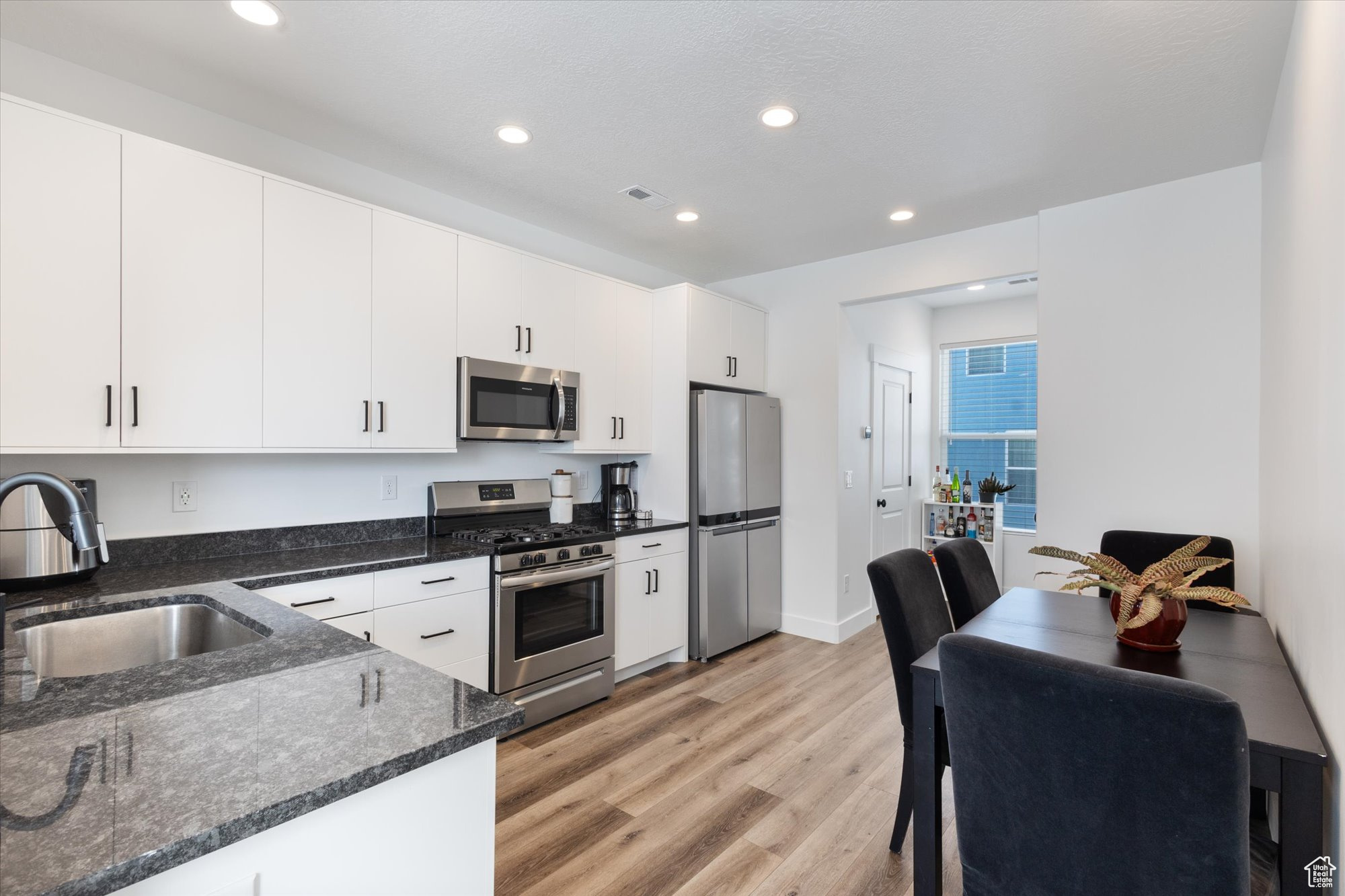 Kitchen with dark stone counters, sink, light hardwood / wood-style floors, stainless steel appliances, and white cabinets