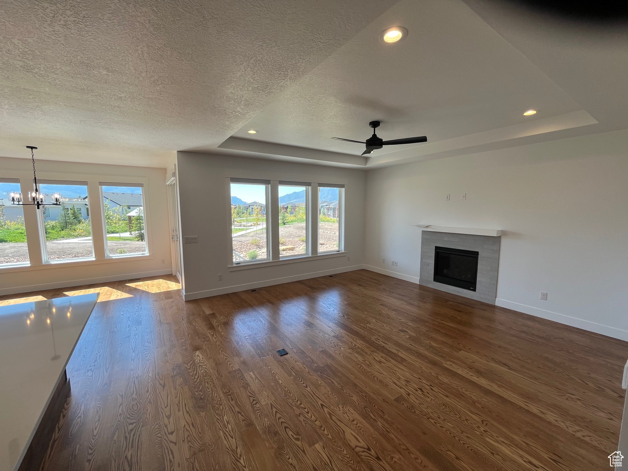 Unfurnished living room with a tray ceiling, ceiling fan with notable chandelier, a fireplace, and dark hardwood / wood-style floors