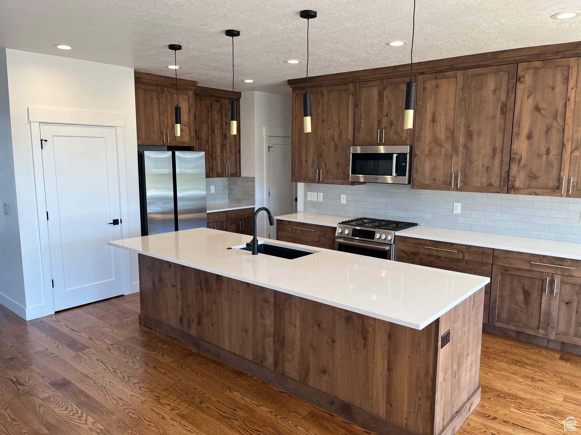 Kitchen with decorative light fixtures, hardwood / wood-style floors, stainless steel appliances, and a center island with sink