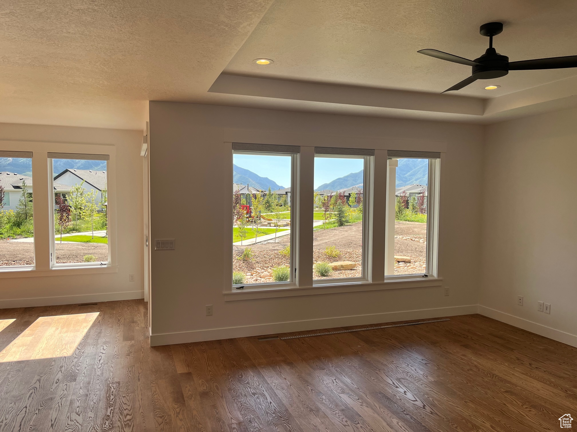 Empty room featuring a mountain view, hardwood / wood-style floors, a raised ceiling, a textured ceiling, and ceiling fan