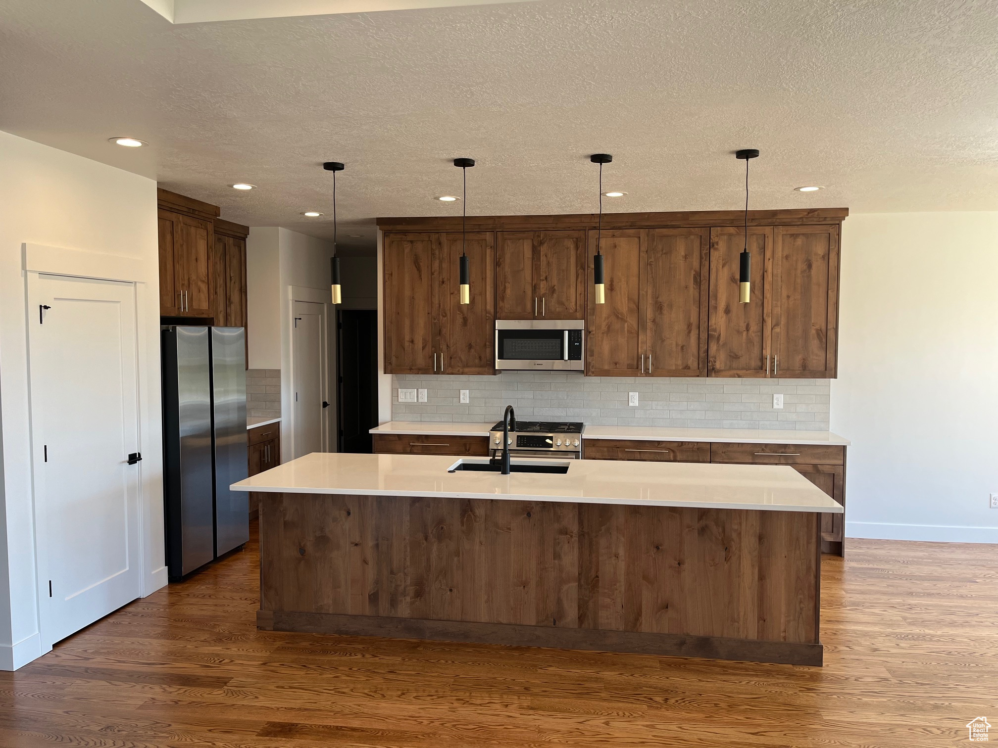 Kitchen featuring a kitchen island with sink, stainless steel appliances, dark hardwood / wood-style flooring, sink, and hanging light fixtures