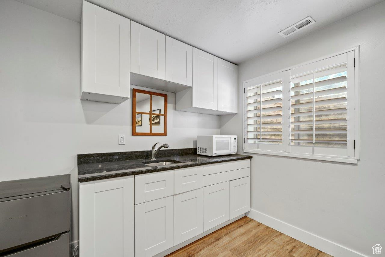 Wetbar/ Kitchenette with white cabinets, dark stone countertops, sink, and light hardwood / wood-style floors