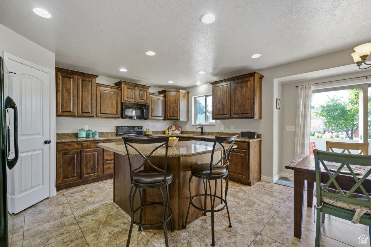 Kitchen with light tile patterned flooring, range, a kitchen island, and a healthy amount of sunlight