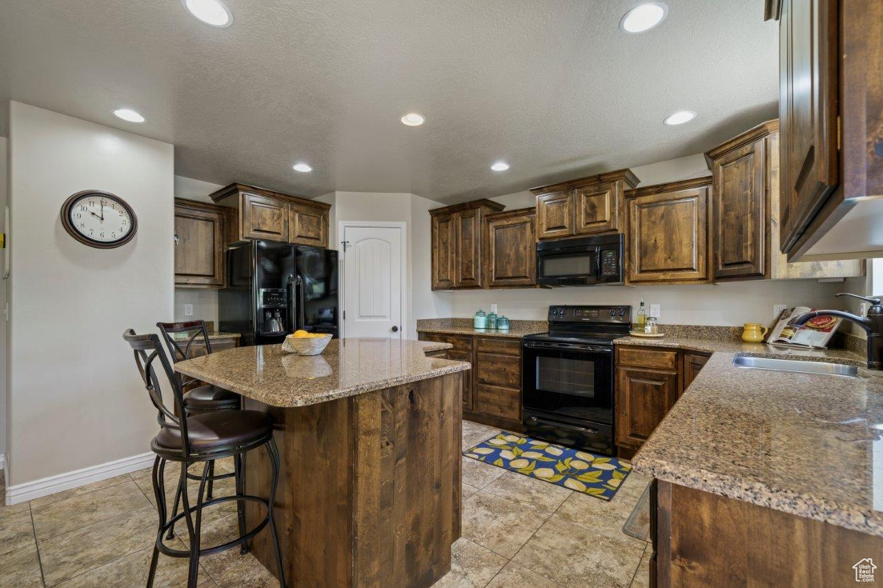 Kitchen with a kitchen island, sink, a breakfast bar area, black appliances, and light tile patterned flooring