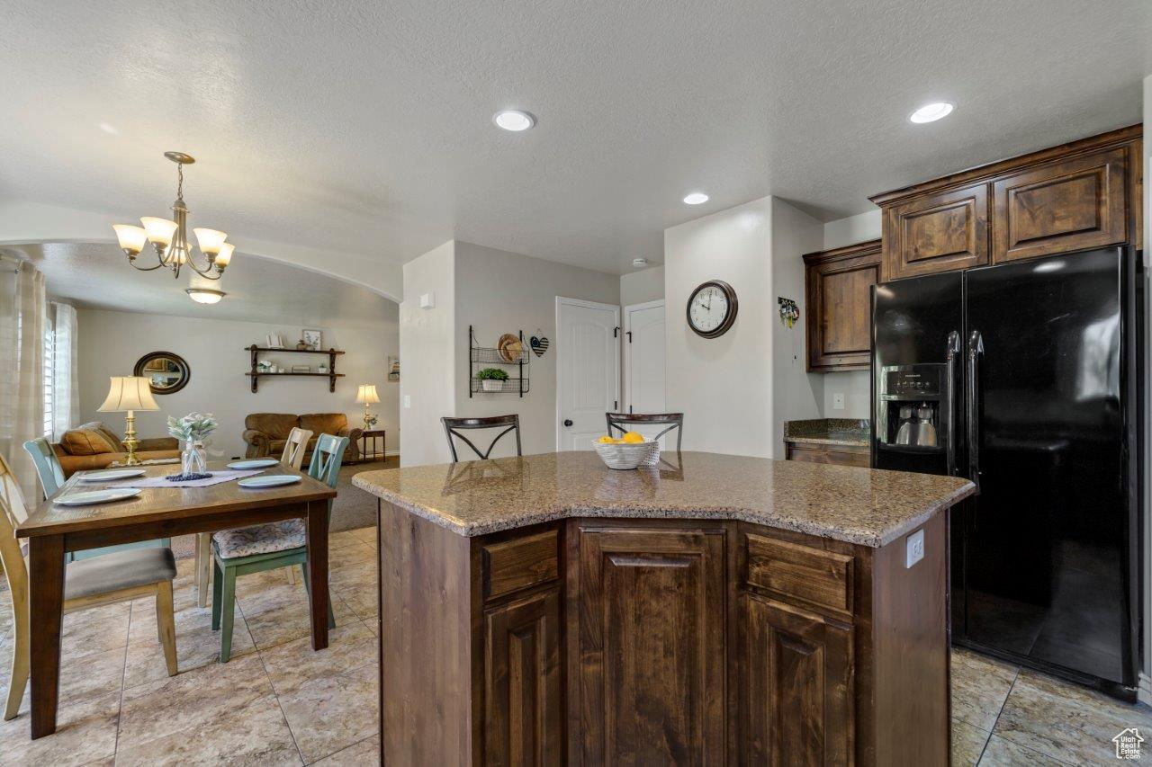 Kitchen with black fridge with ice dispenser, a center island, light tile patterned floors, and light stone counters