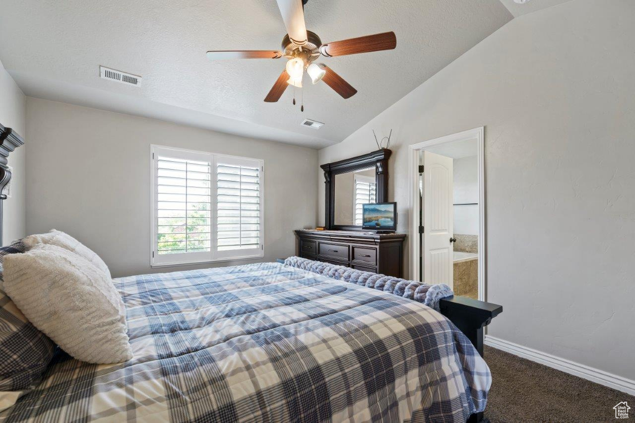 Bedroom featuring ceiling fan, carpet, vaulted ceiling, and ensuite bathroom