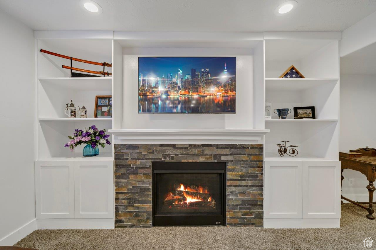 Room details featuring carpet, a stone fireplace, and built in features