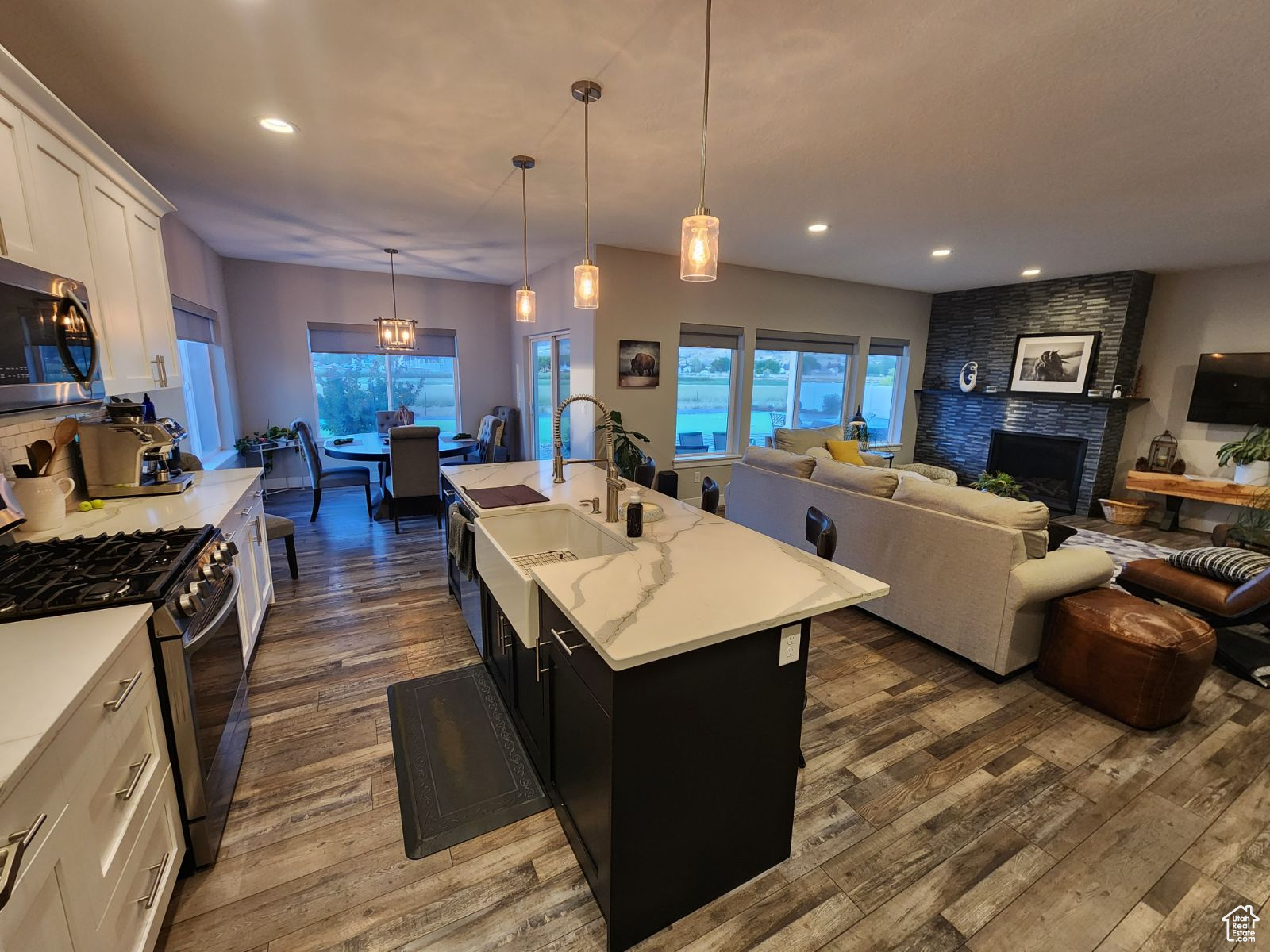 Kitchen featuring gas range, a fireplace, pendant lighting, a kitchen island with sink, and dark wood-type flooring