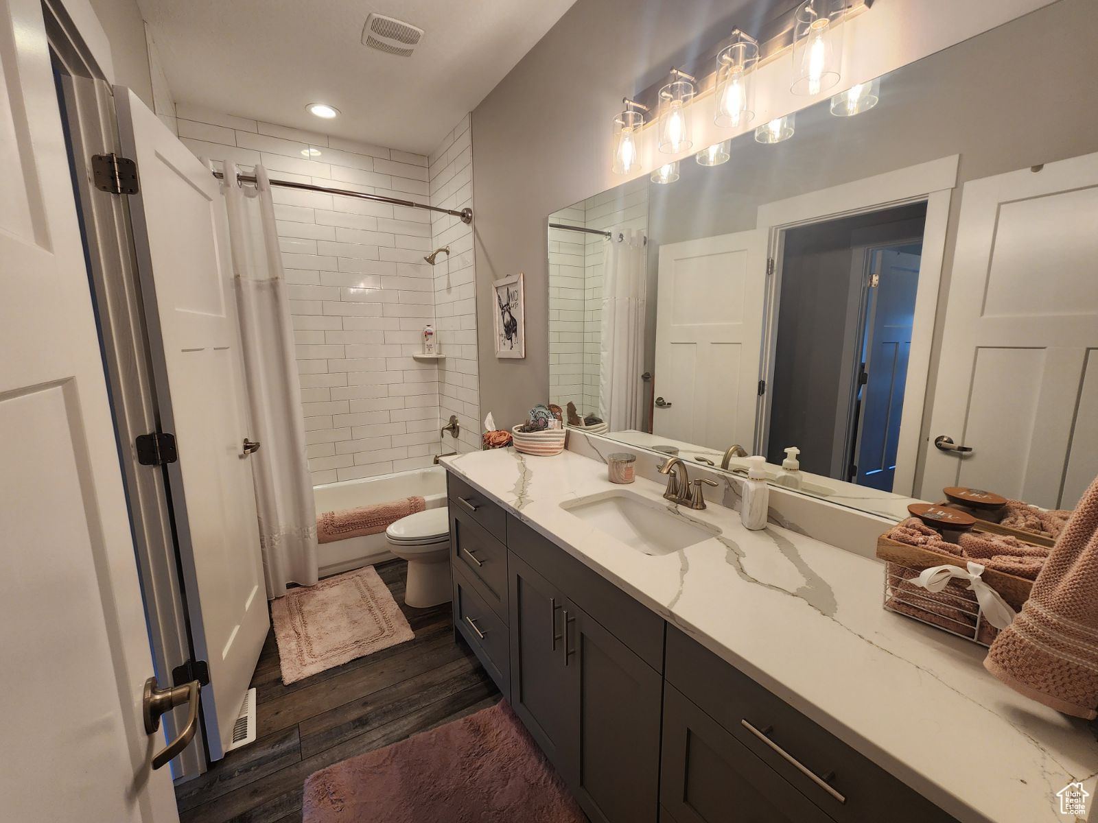 Full bathroom with wood-type flooring, shower / bath combination with curtain, vanity, and toilet