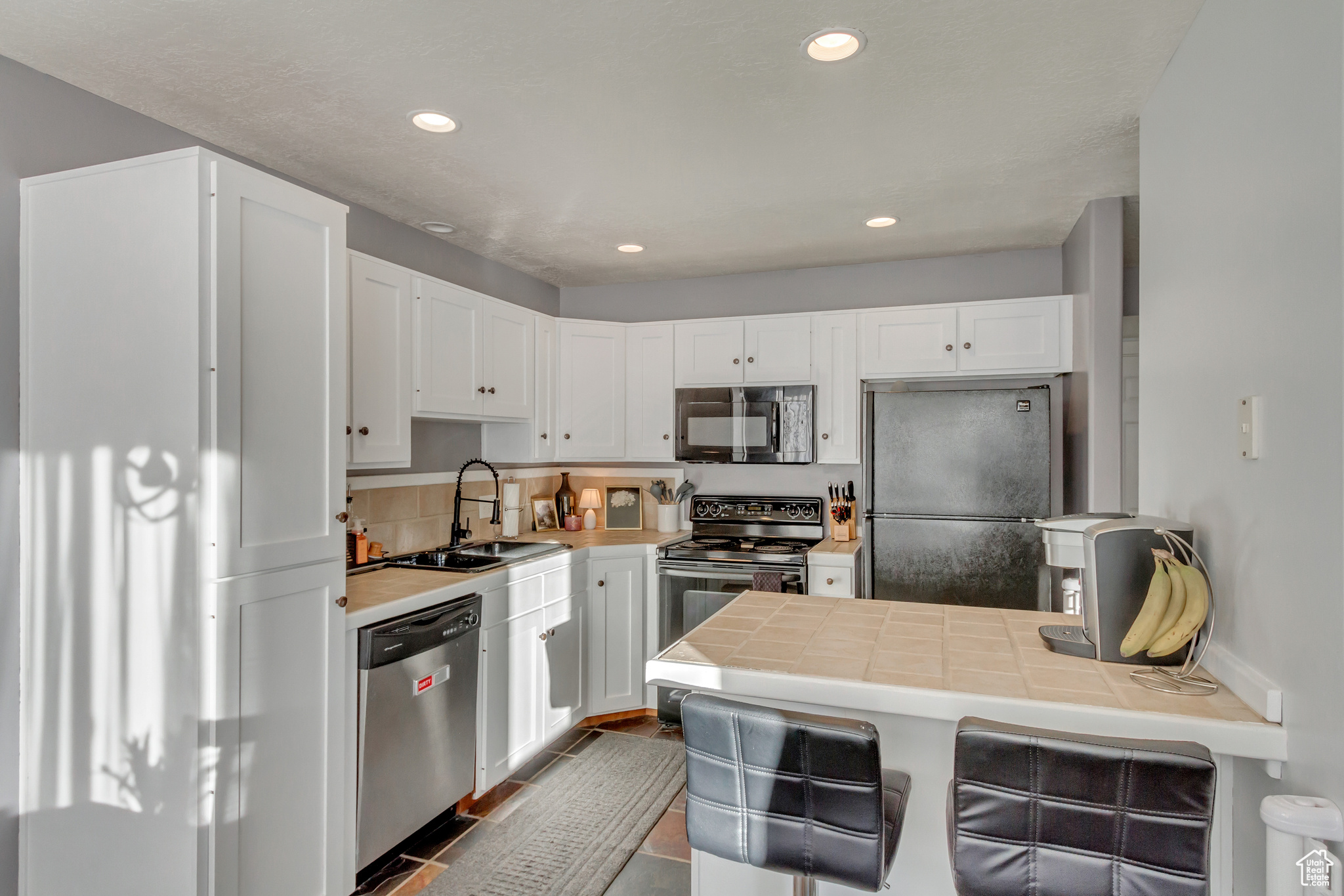 Kitchen with tile countertops, white cabinetry, and appliances with stainless steel finishes