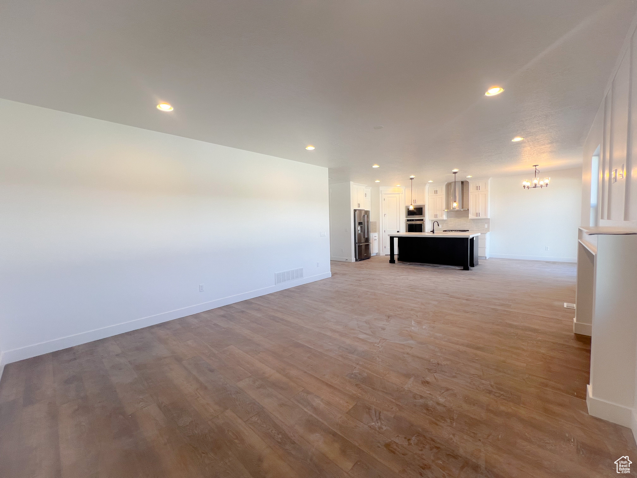 Unfurnished living room with sink, light wood-type flooring, and a notable chandelier