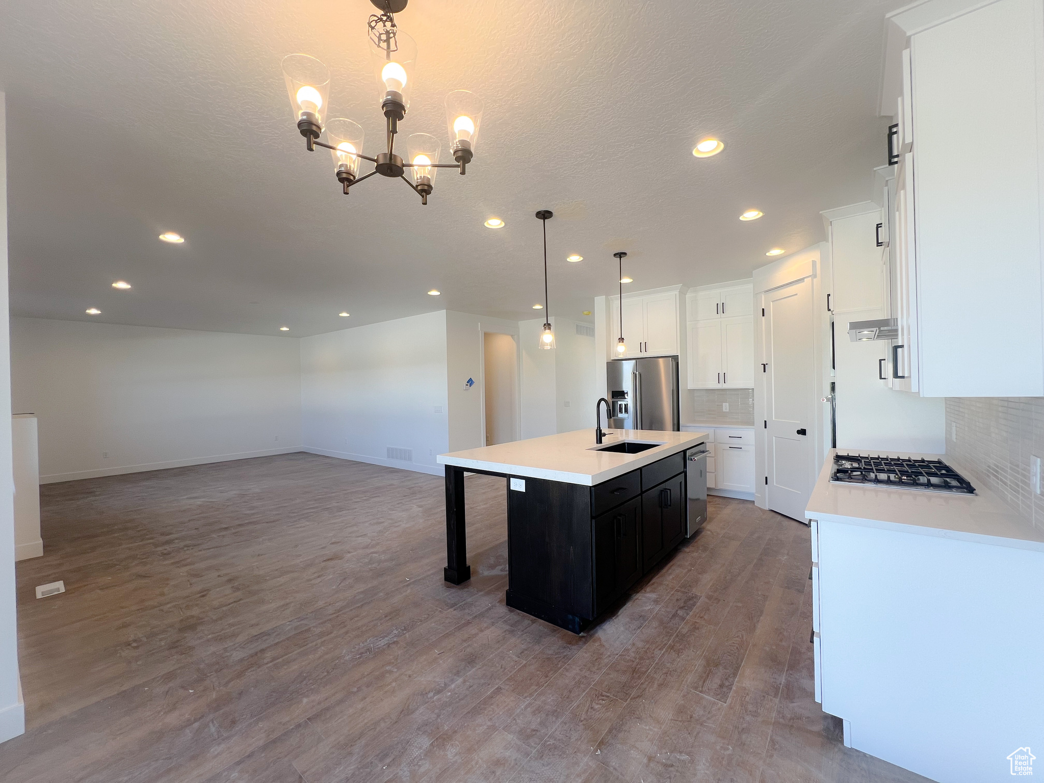 Kitchen featuring tasteful backsplash, hanging light fixtures, a kitchen island with sink, wood-type flooring, and appliances with stainless steel finishes