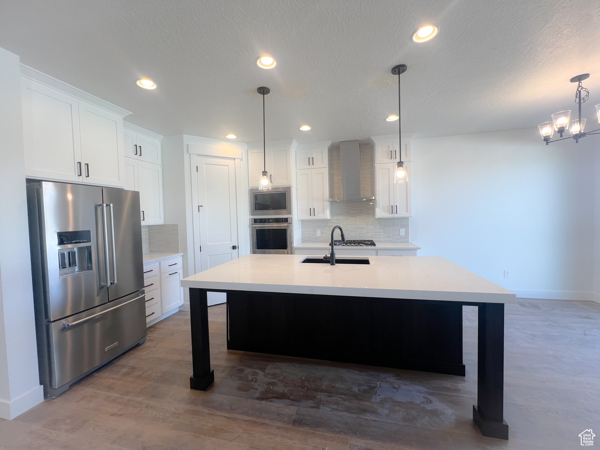 Kitchen featuring stainless steel appliances, wall chimney exhaust hood, tasteful backsplash, an island with sink, and hardwood / wood-style flooring