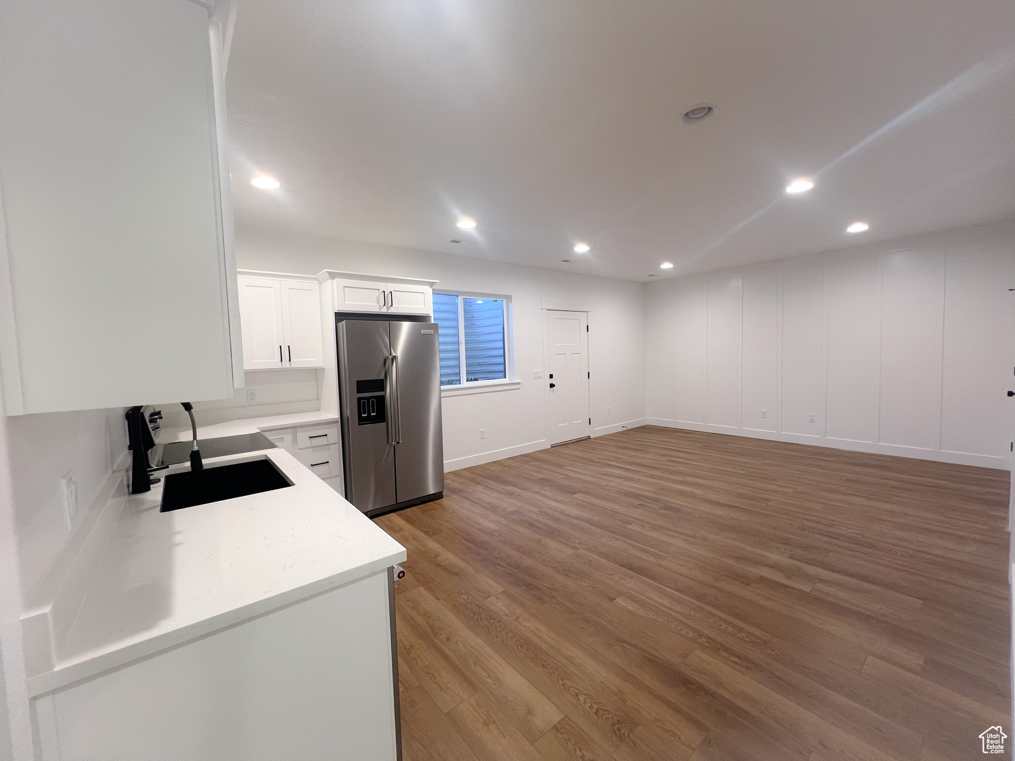 Kitchen with stainless steel fridge with ice dispenser, sink, light wood-type flooring, and white cabinets