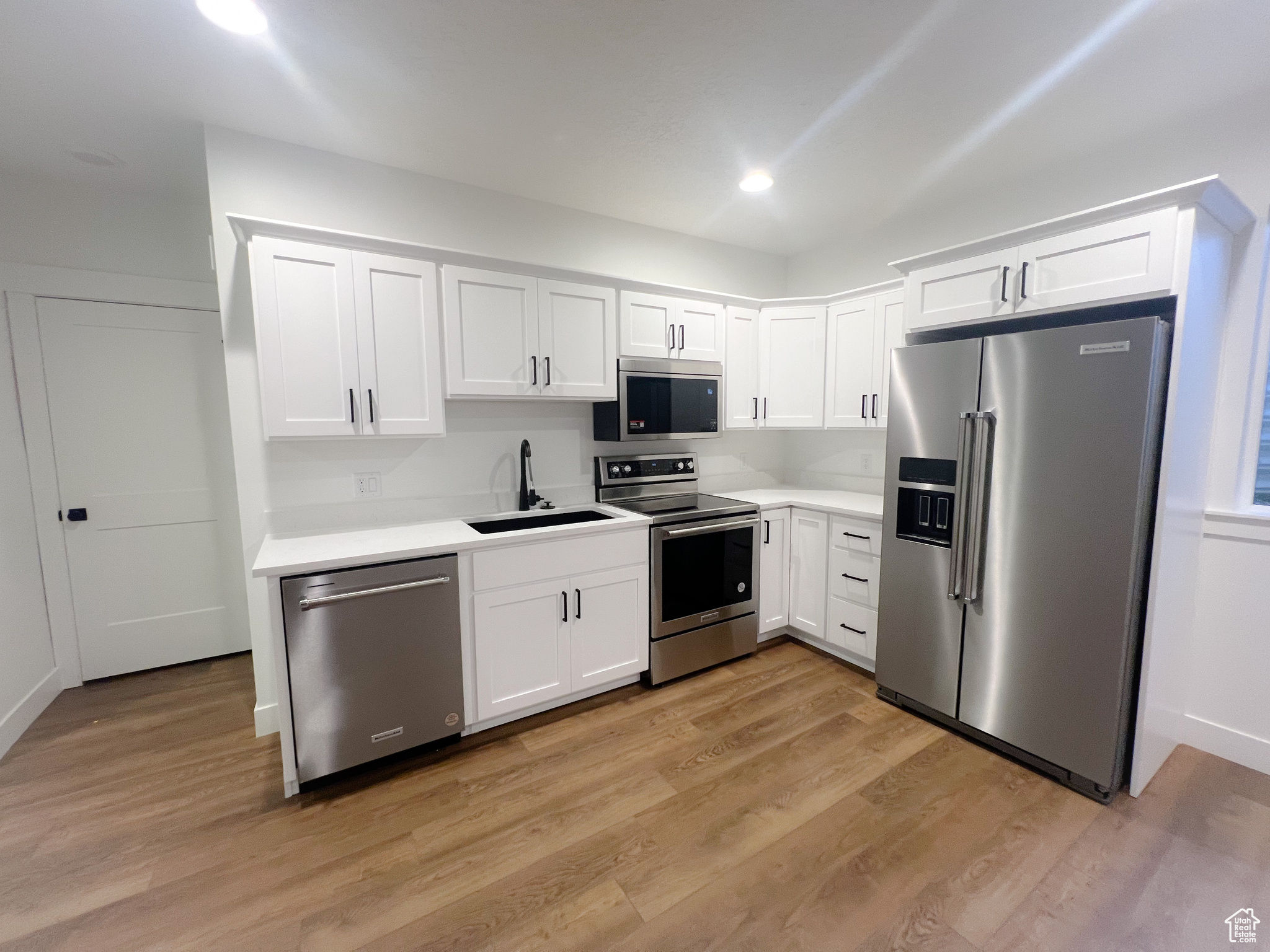 Kitchen featuring sink, stainless steel appliances, light hardwood / wood-style floors, and white cabinets