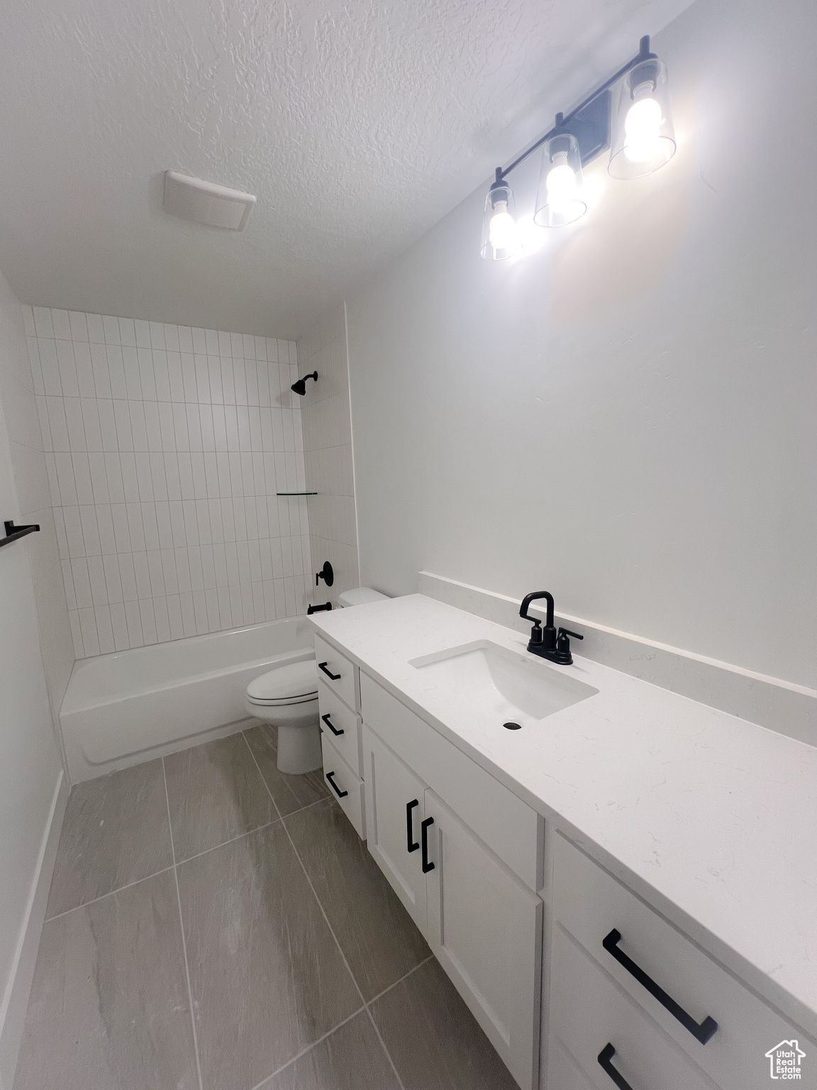 Full bathroom with toilet, tile patterned flooring, vanity, a textured ceiling, and tiled shower / bath