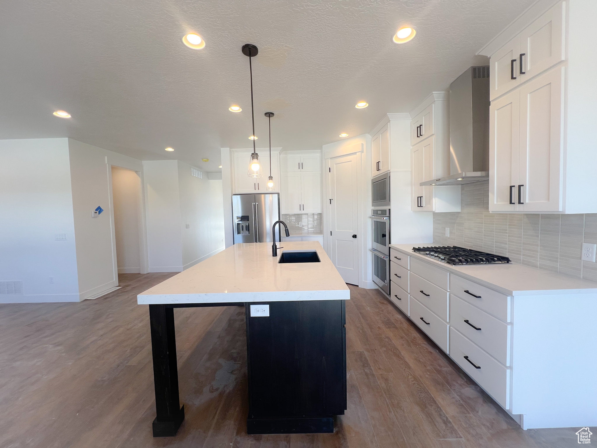 Kitchen with wall chimney range hood, decorative backsplash, appliances with stainless steel finishes, sink, and a center island with sink