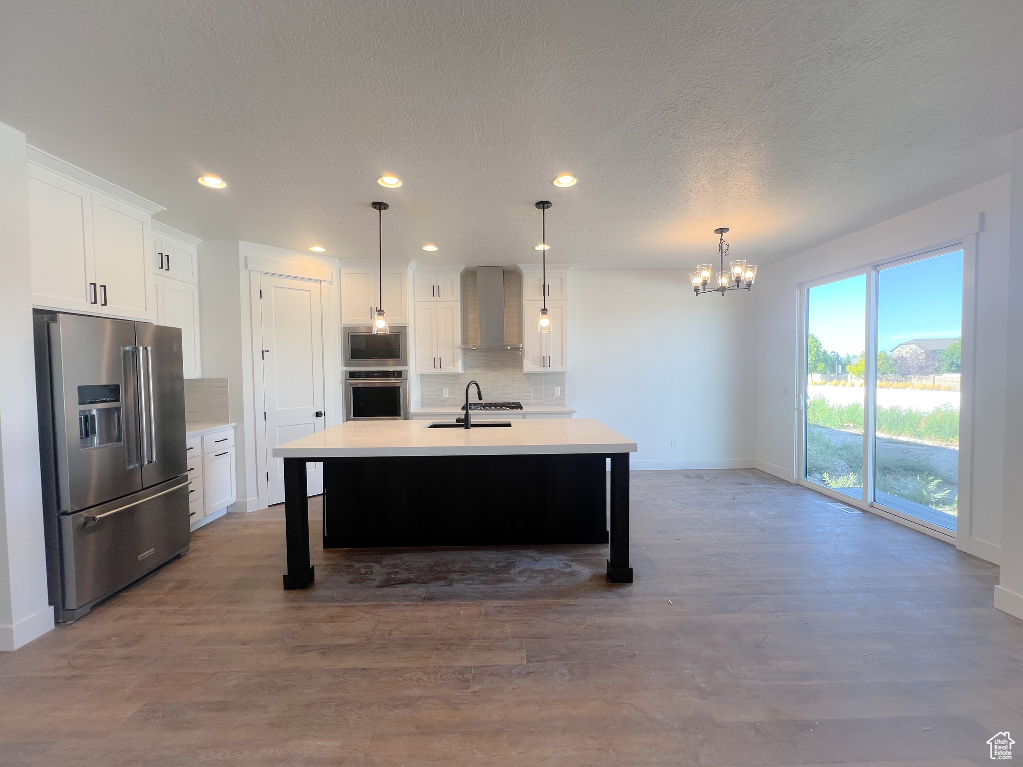 Kitchen with wall chimney range hood, a healthy amount of sunlight, tasteful backsplash, hardwood / wood-style floors, and stainless steel appliances