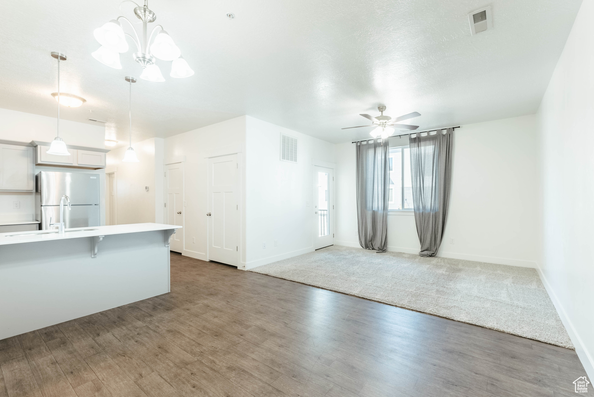 Unfurnished living room with sink, ceiling fan with notable chandelier, and hardwood / wood-style flooring