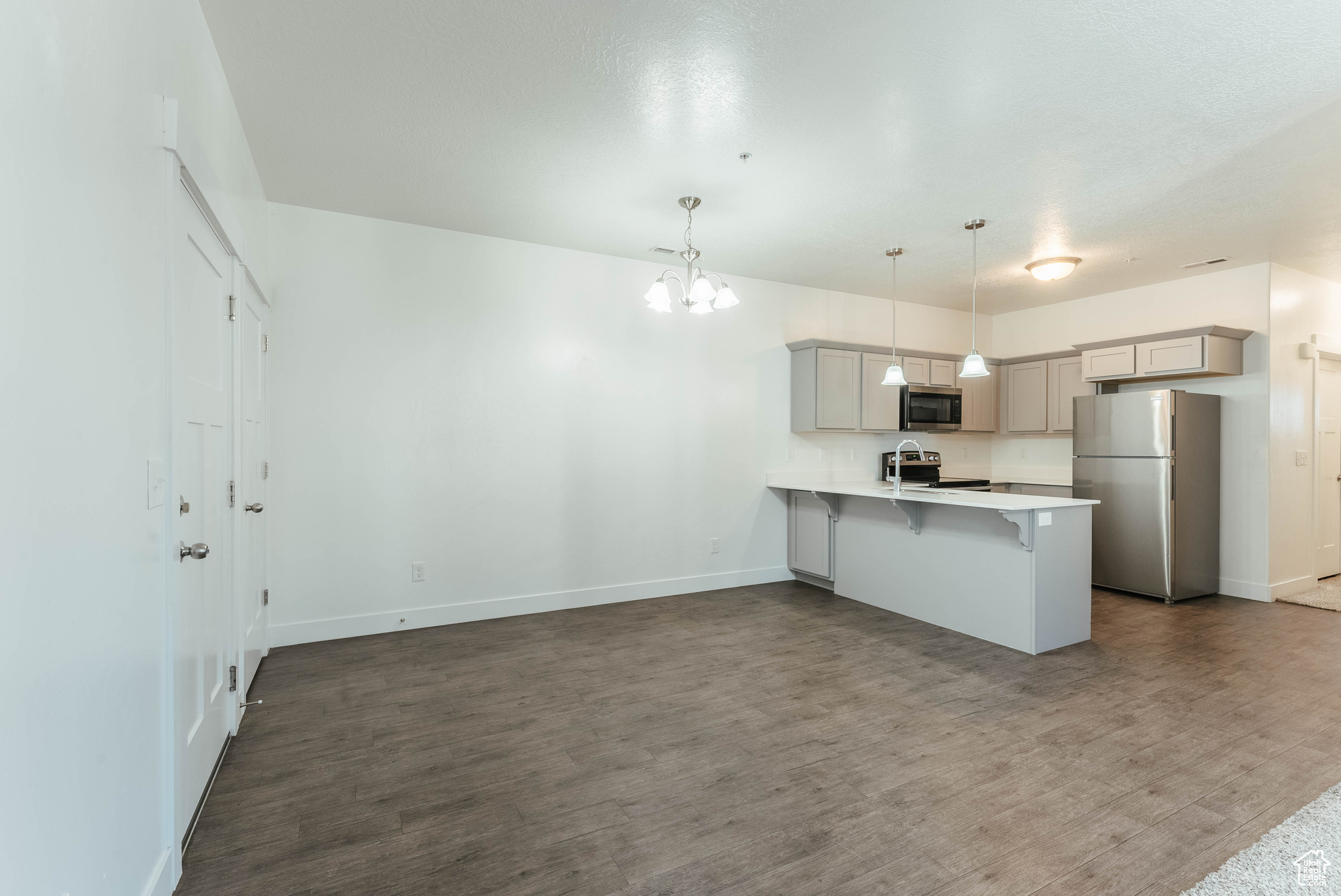 Kitchen with a kitchen breakfast bar, hanging light fixtures, appliances with stainless steel finishes, wood-type flooring, and kitchen peninsula