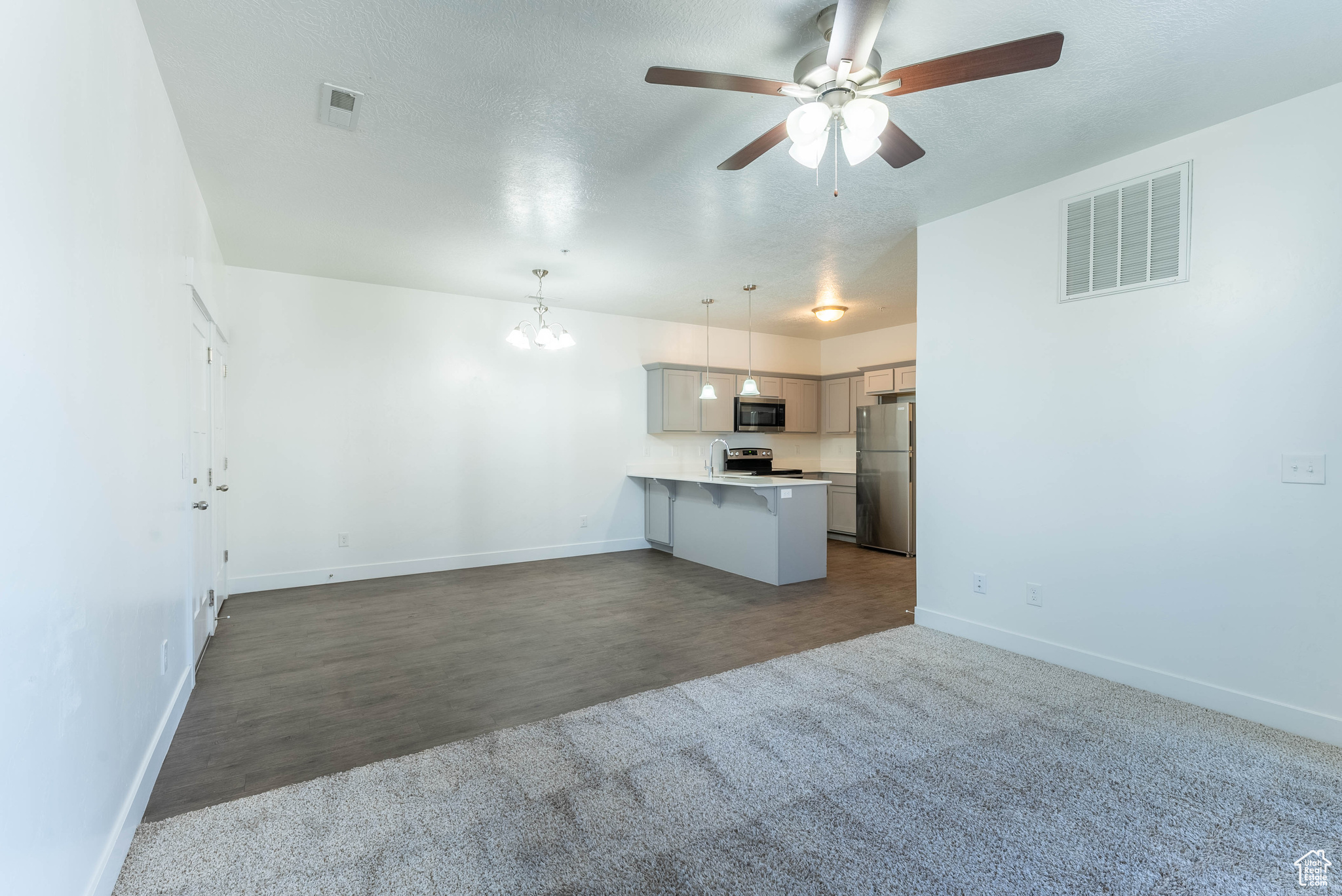 Unfurnished living room featuring ceiling fan with notable chandelier and dark hardwood / wood-style flooring