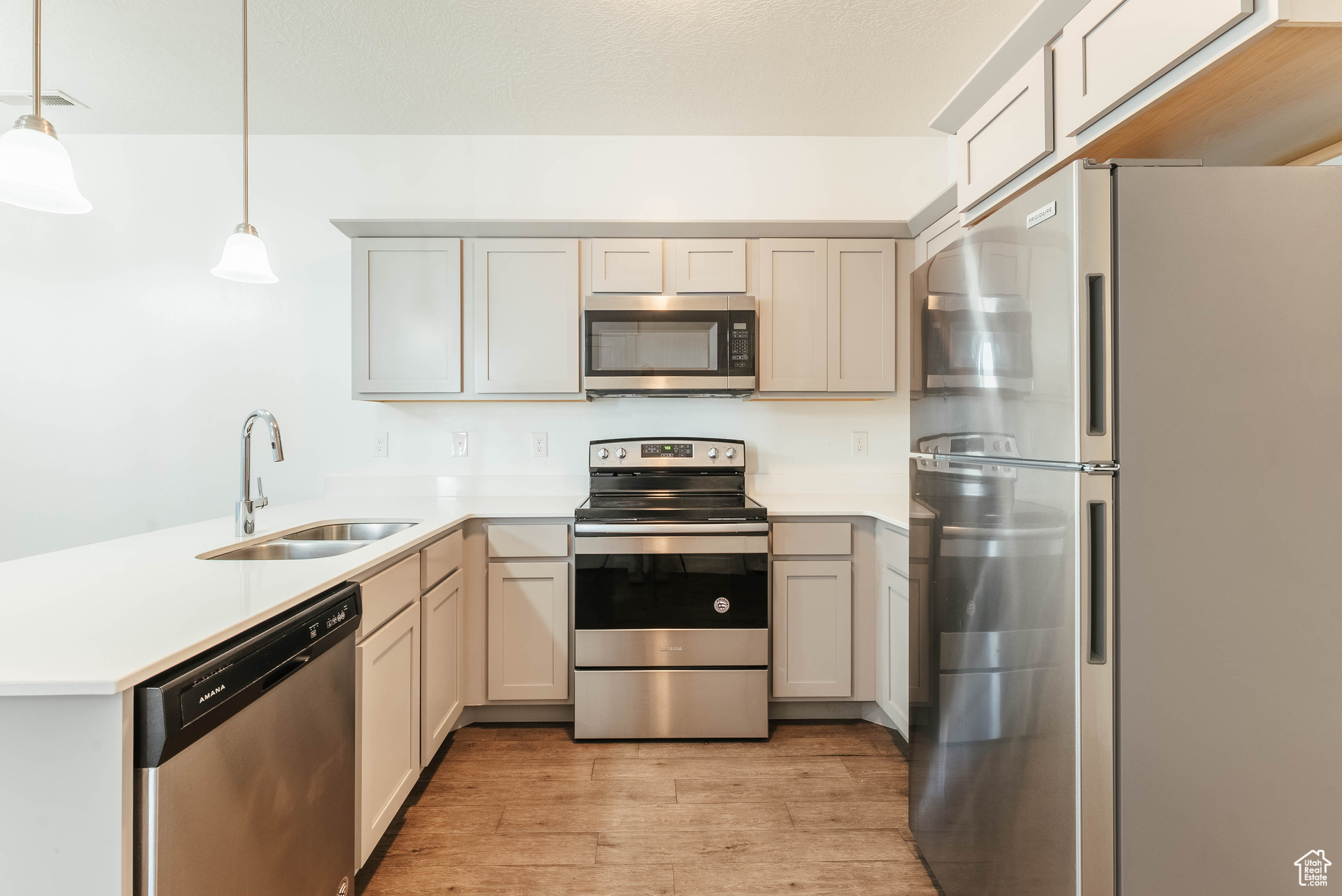 Kitchen with appliances with stainless steel finishes, light hardwood / wood-style floors, sink, gray cabinetry, and pendant lighting