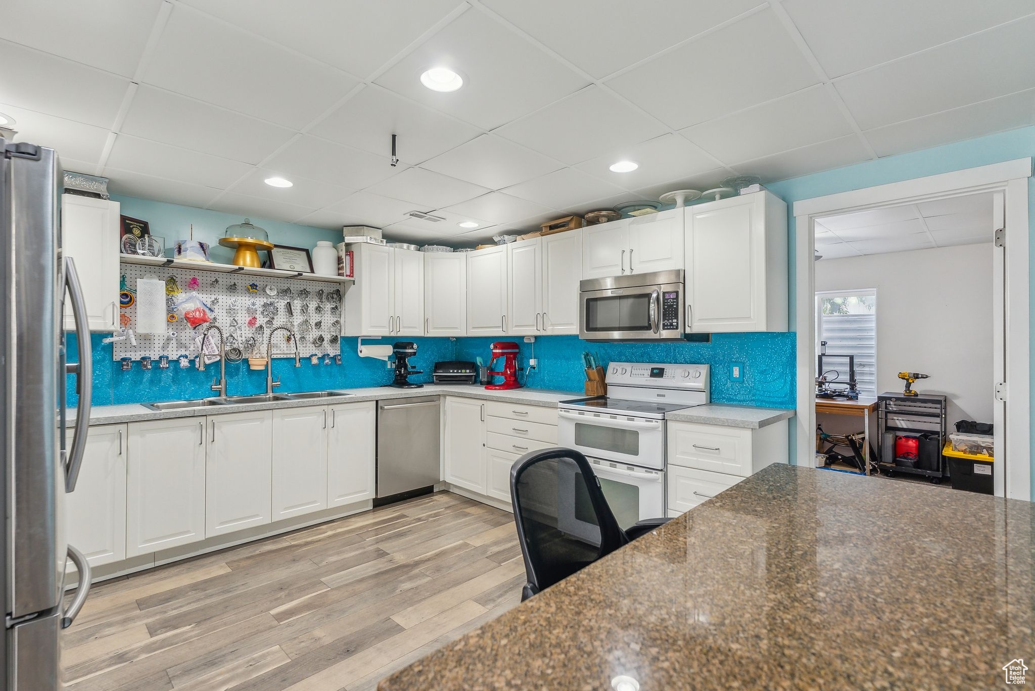 Kitchen featuring light wood-type flooring, white cabinets, appliances with stainless steel finishes, sink, and dark stone countertops