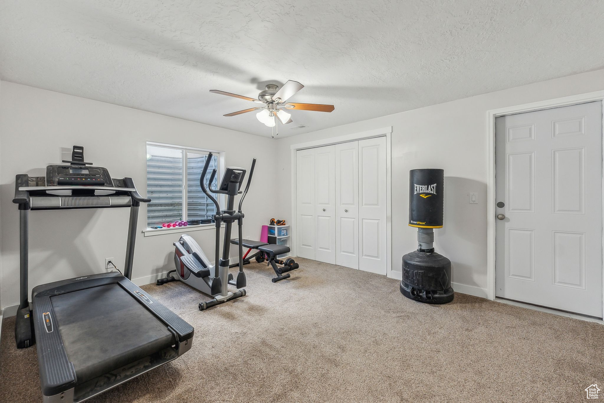 Exercise area featuring ceiling fan, carpet flooring, and a textured ceiling