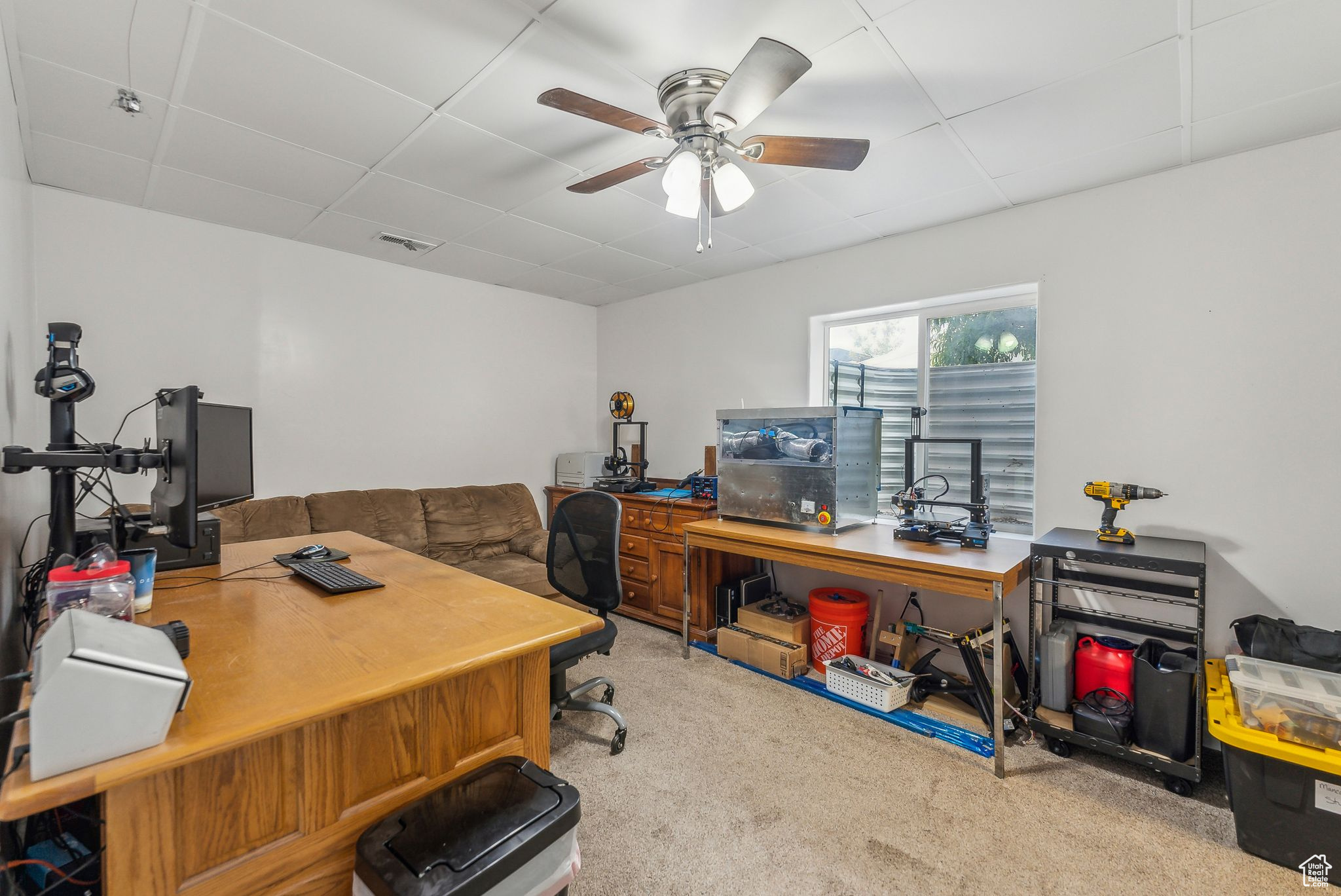 Office area with a paneled ceiling, ceiling fan, and light colored carpet