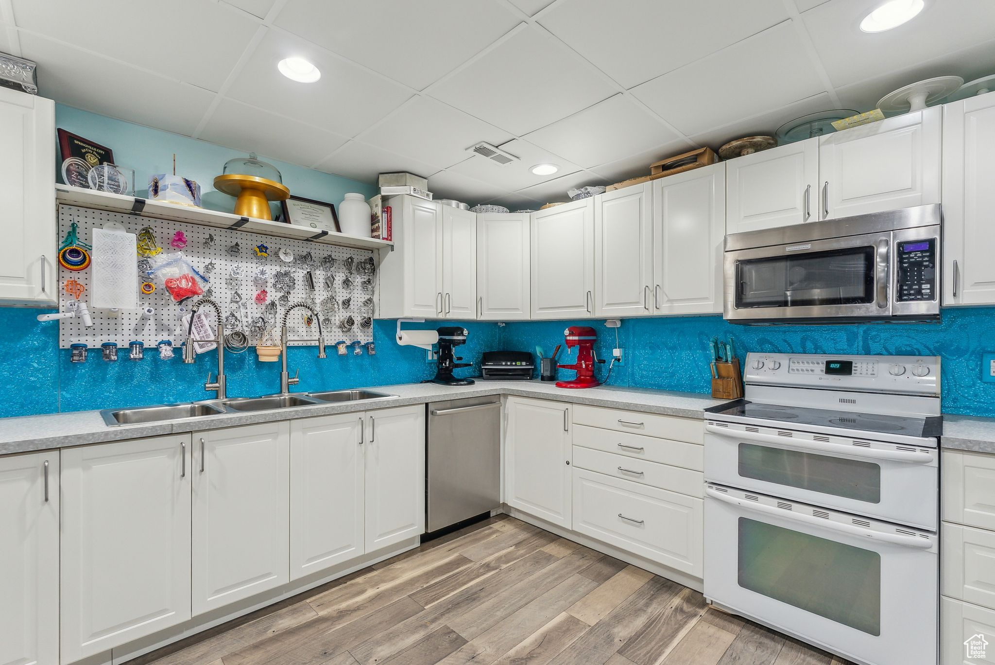 Kitchen featuring a drop ceiling, white cabinets, light hardwood / wood-style floors, sink, and stainless steel appliances