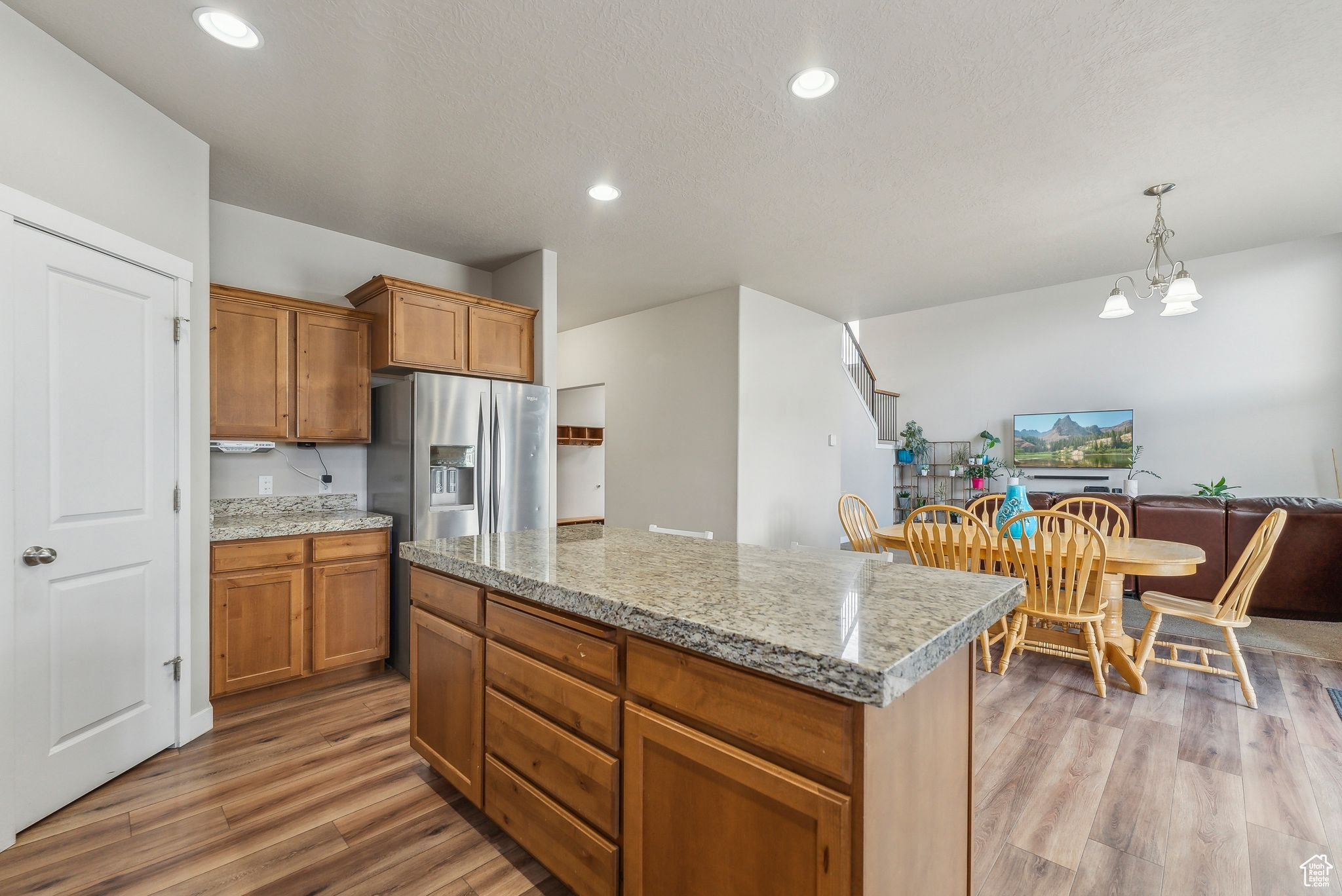 Kitchen with pendant lighting, hardwood / wood-style floors, stainless steel fridge with ice dispenser, an inviting chandelier, and a center island